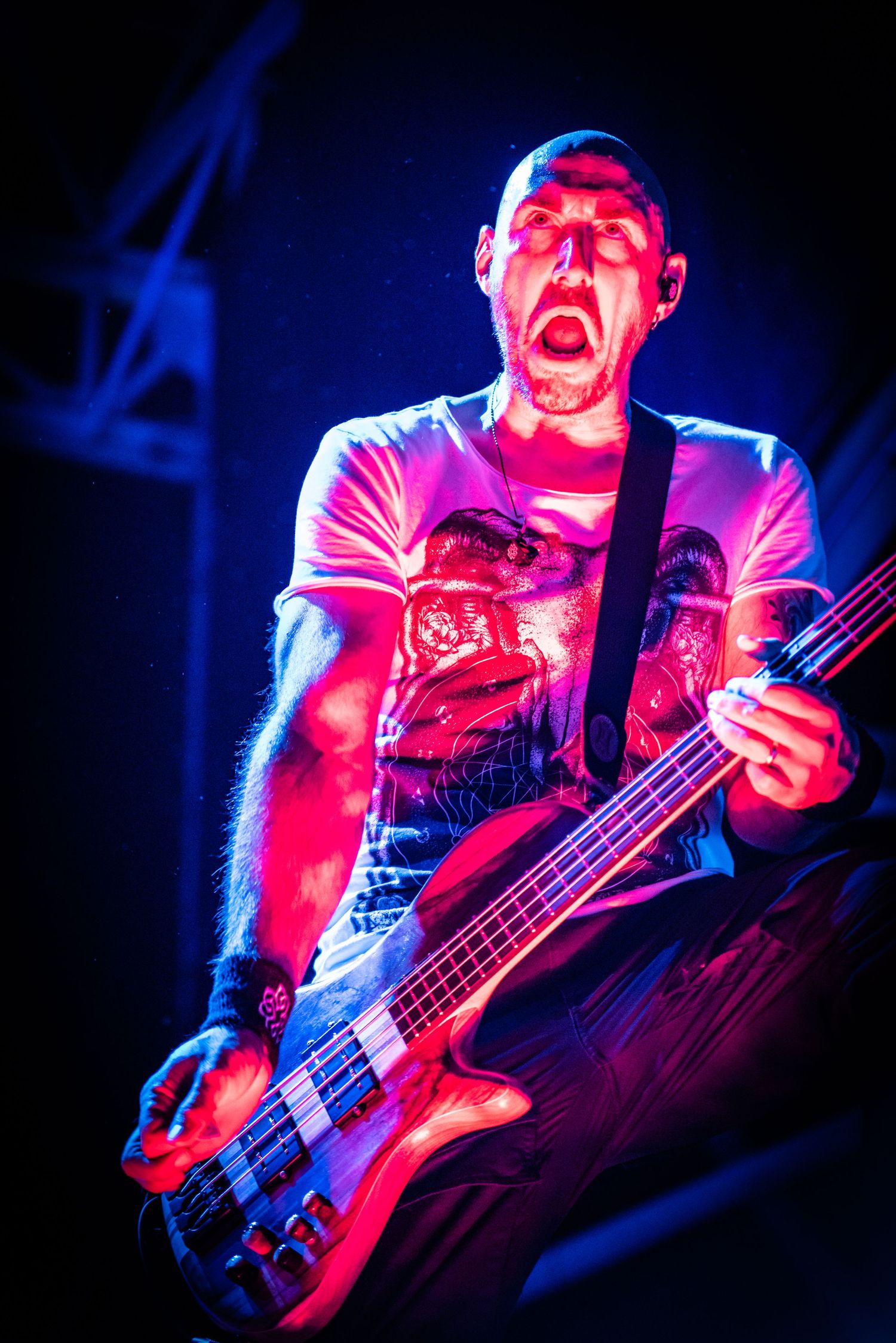 Bass player performs on stage illuminated by dramatic red and blue lighting during an energetic concert performance.