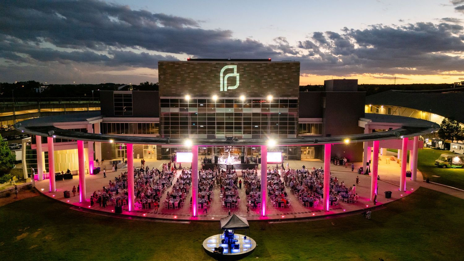 An outdoor amphitheater illuminated with pink lights during sunset with socially distanced seating arrangements.
