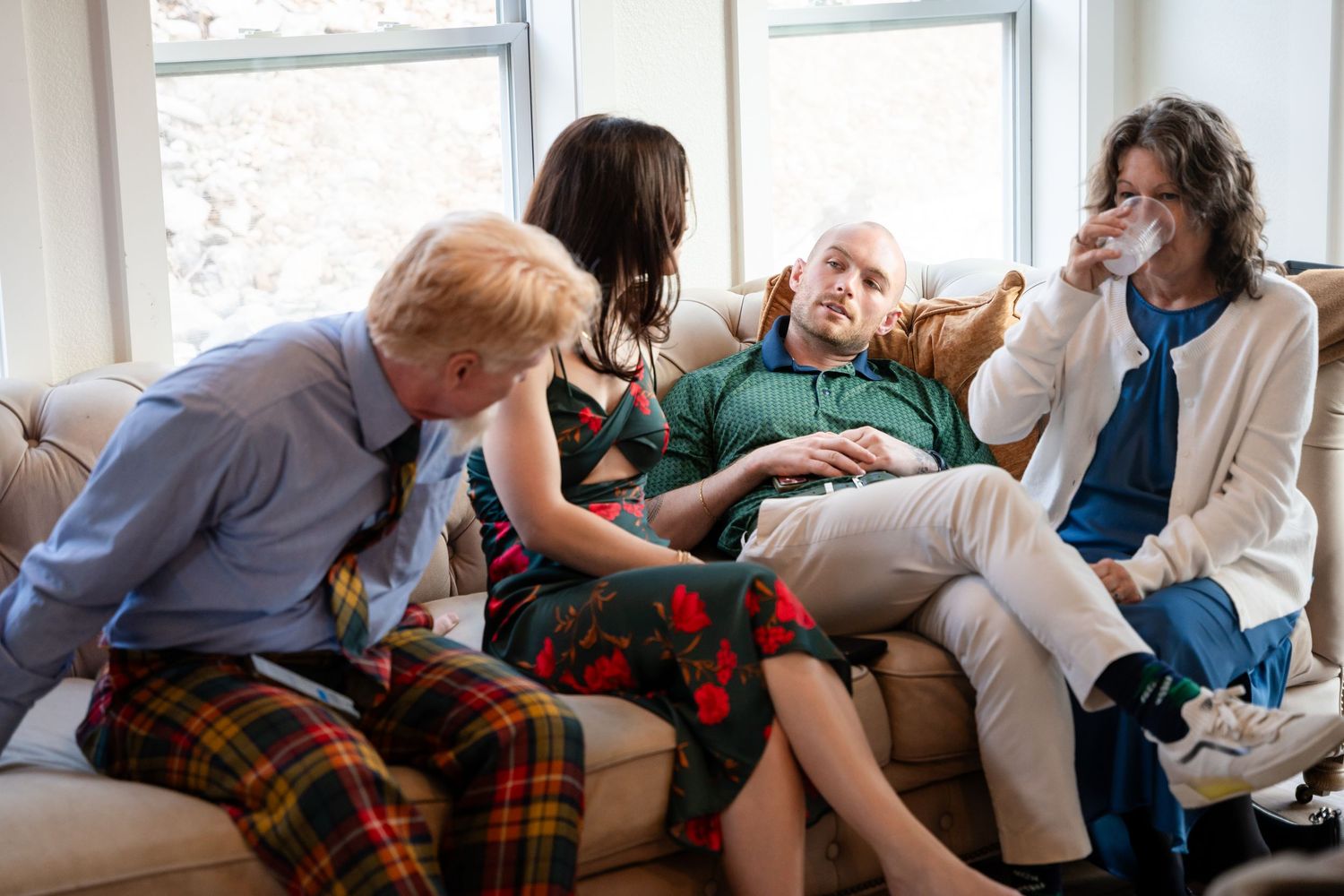 Four people sitting together on a couch in a bright living room, engaged in warm conversation.