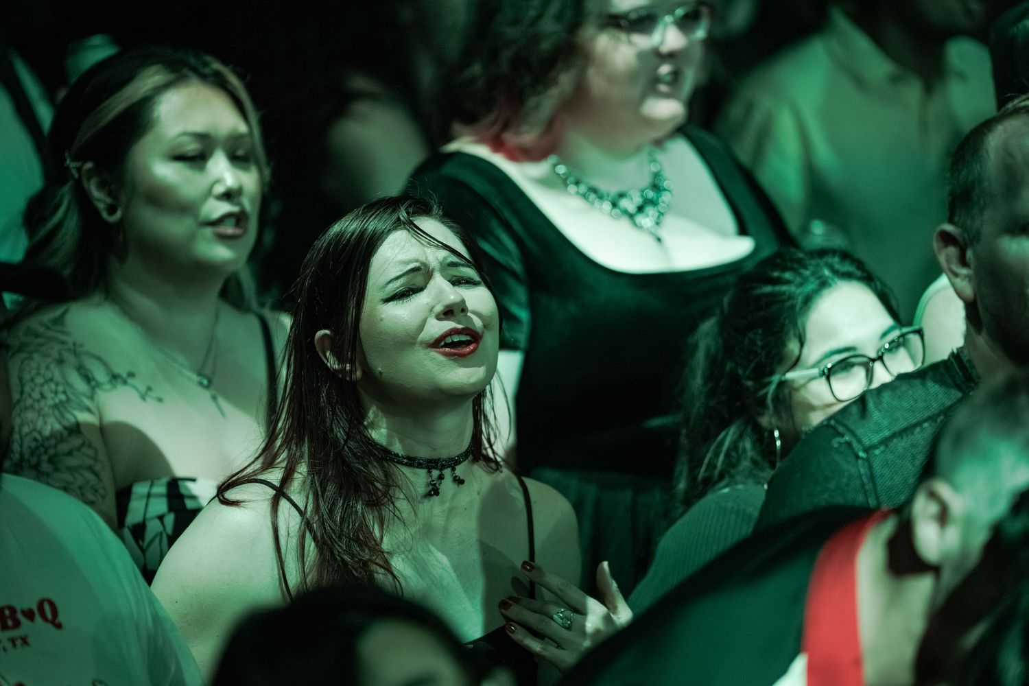 Group of gothic women in dark attire under green lights at a concert event.