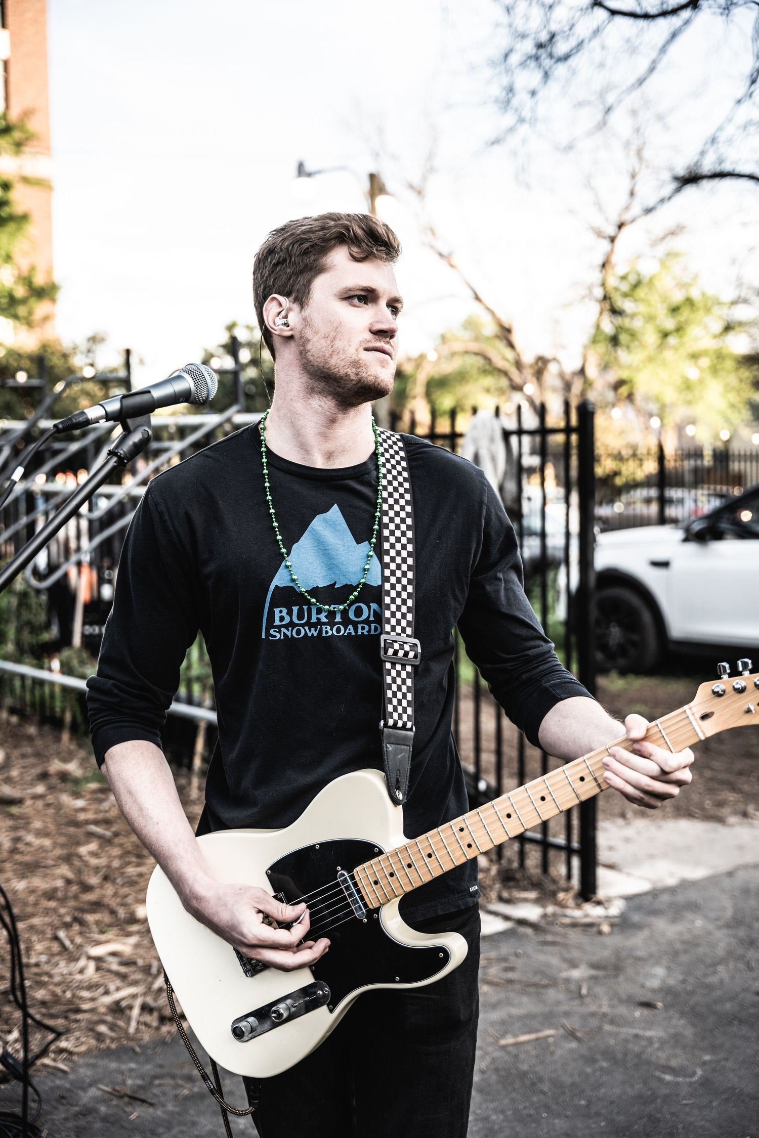 Musician playing white electric guitar at outdoor venue with black mountain design shirt.