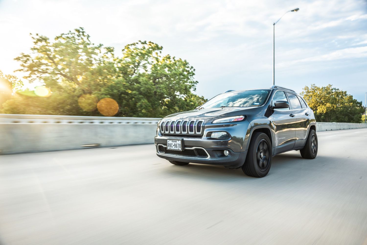 Jeep Cherokee SUV driving on a highway during sunset with lens flare and trees in background.
