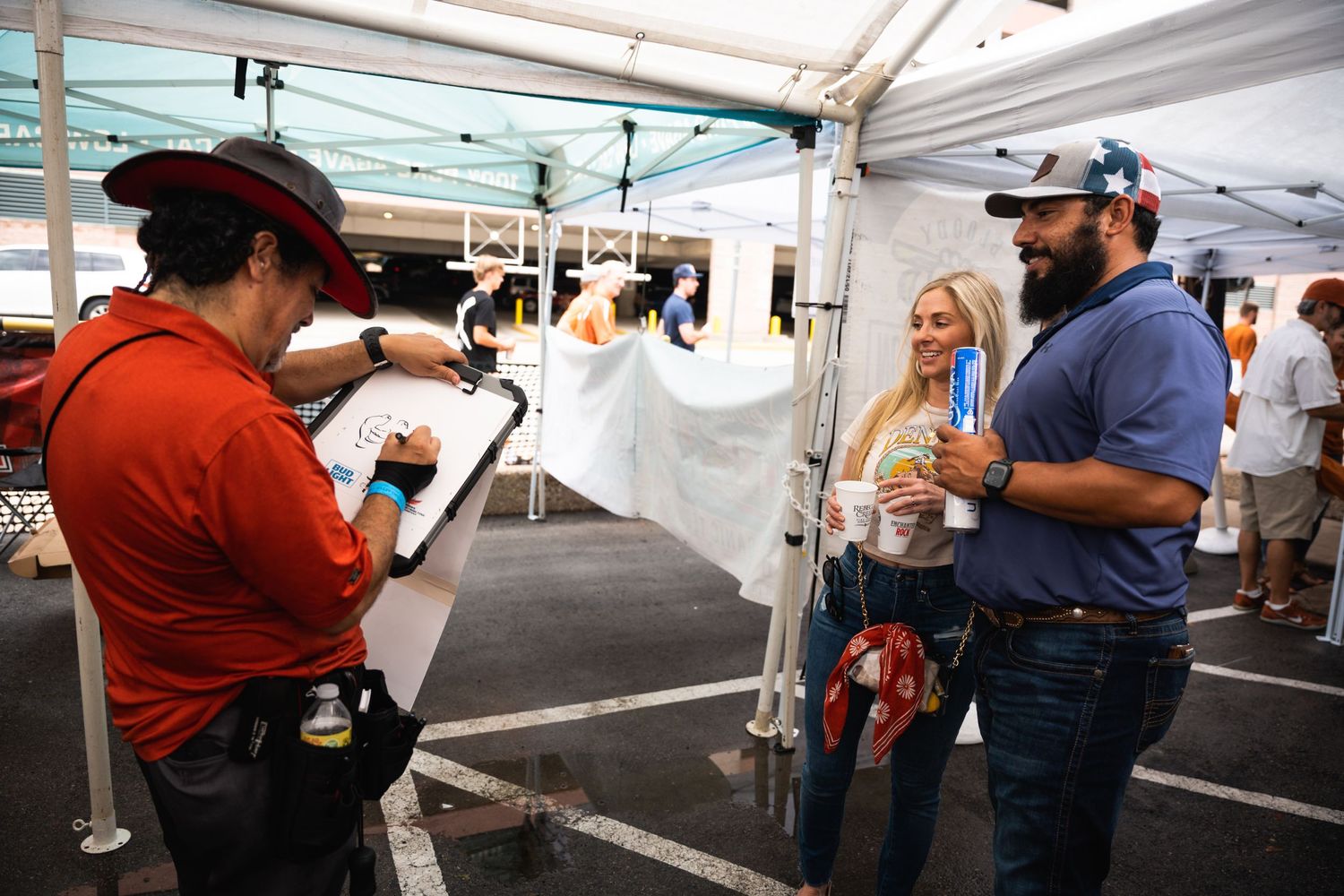People interacting at a covered outdoor vendor booth during a festival or event.
