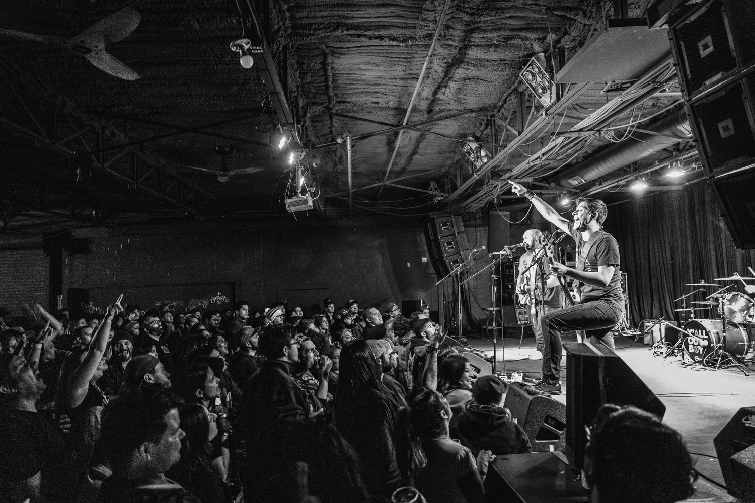 Band plays energetic show on elevated stage with crowd raising hands in black and white photography.