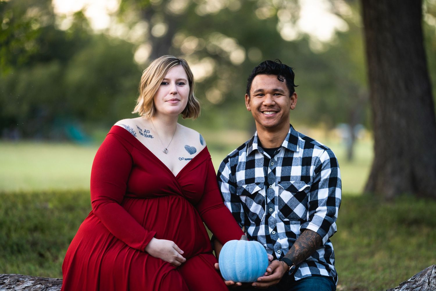 Outdoor maternity photo with couple holding blue pumpkin in park setting.