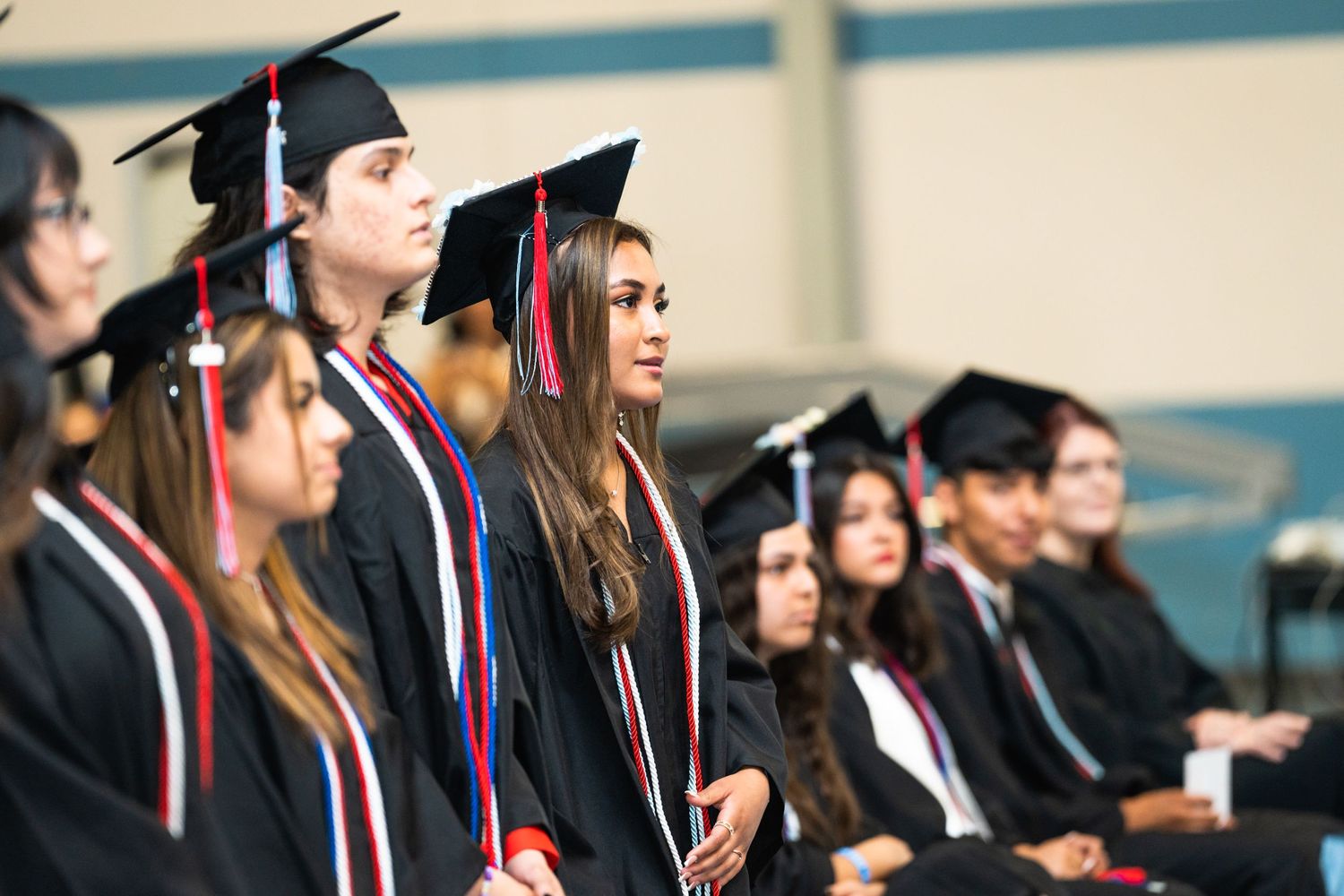 Row of graduates in black caps and gowns sitting during graduation ceremony.