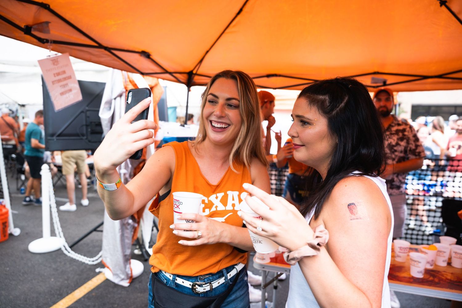 Two attendees in casual attire enjoying drinks and laughing at an outdoor festival.