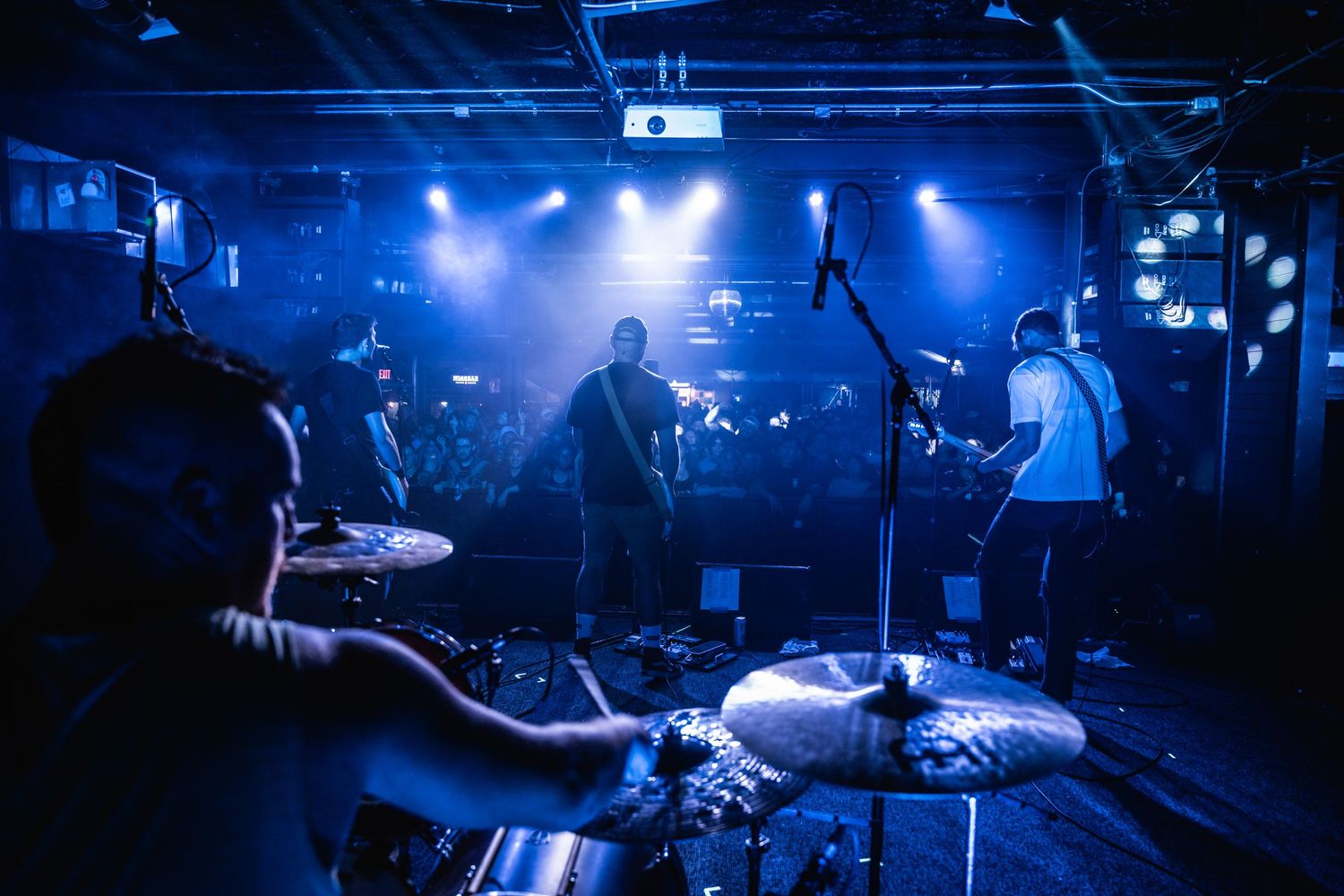 Band performs on dimly lit stage with blue atmospheric lighting and drum kit in foreground.