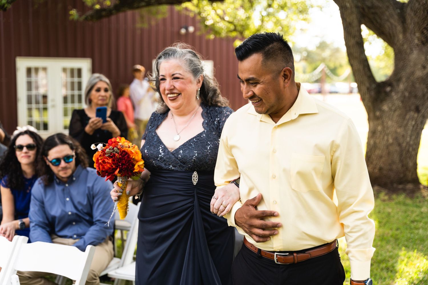 A couple shares a joyful moment at an outdoor celebration with guests seated in the background.