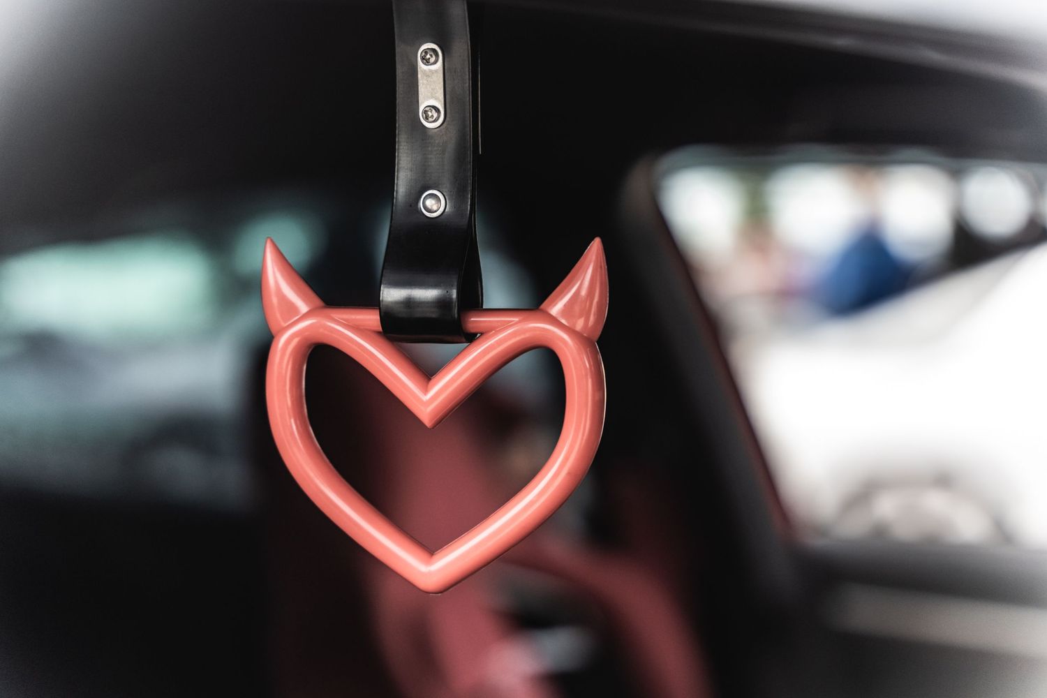 A neon heart-shaped ornament with devil horns hanging from a car mirror.