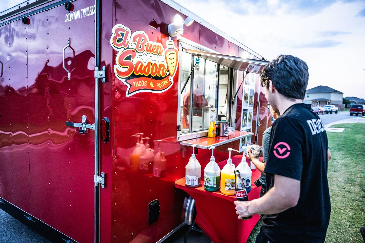 Red food truck vendor serving colorful beverages at outdoor event.