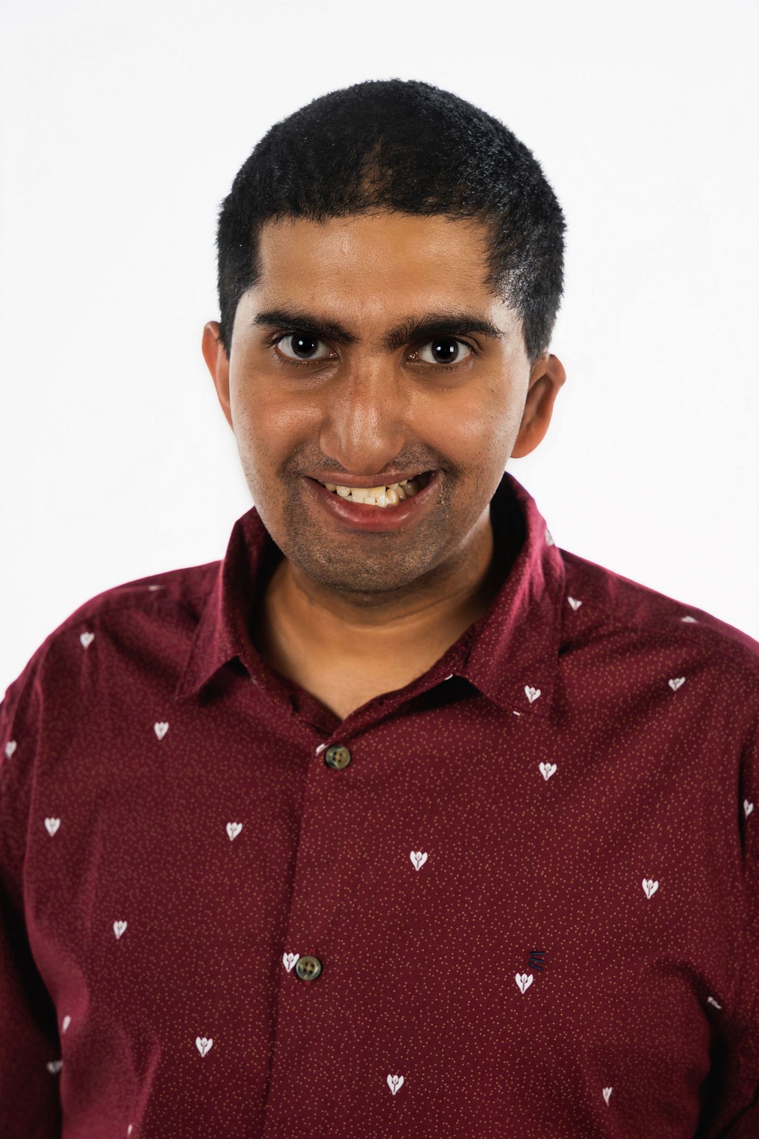 Man wearing burgundy shirt with small heart pattern smiling at camera against white background.