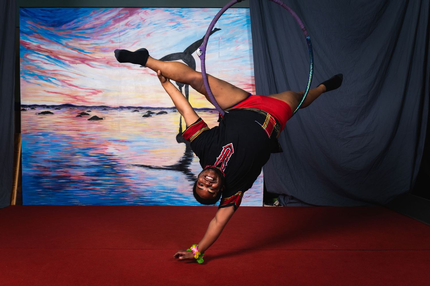 Performer demonstrates impressive strength and flexibility in an aerial dance move on red floor.