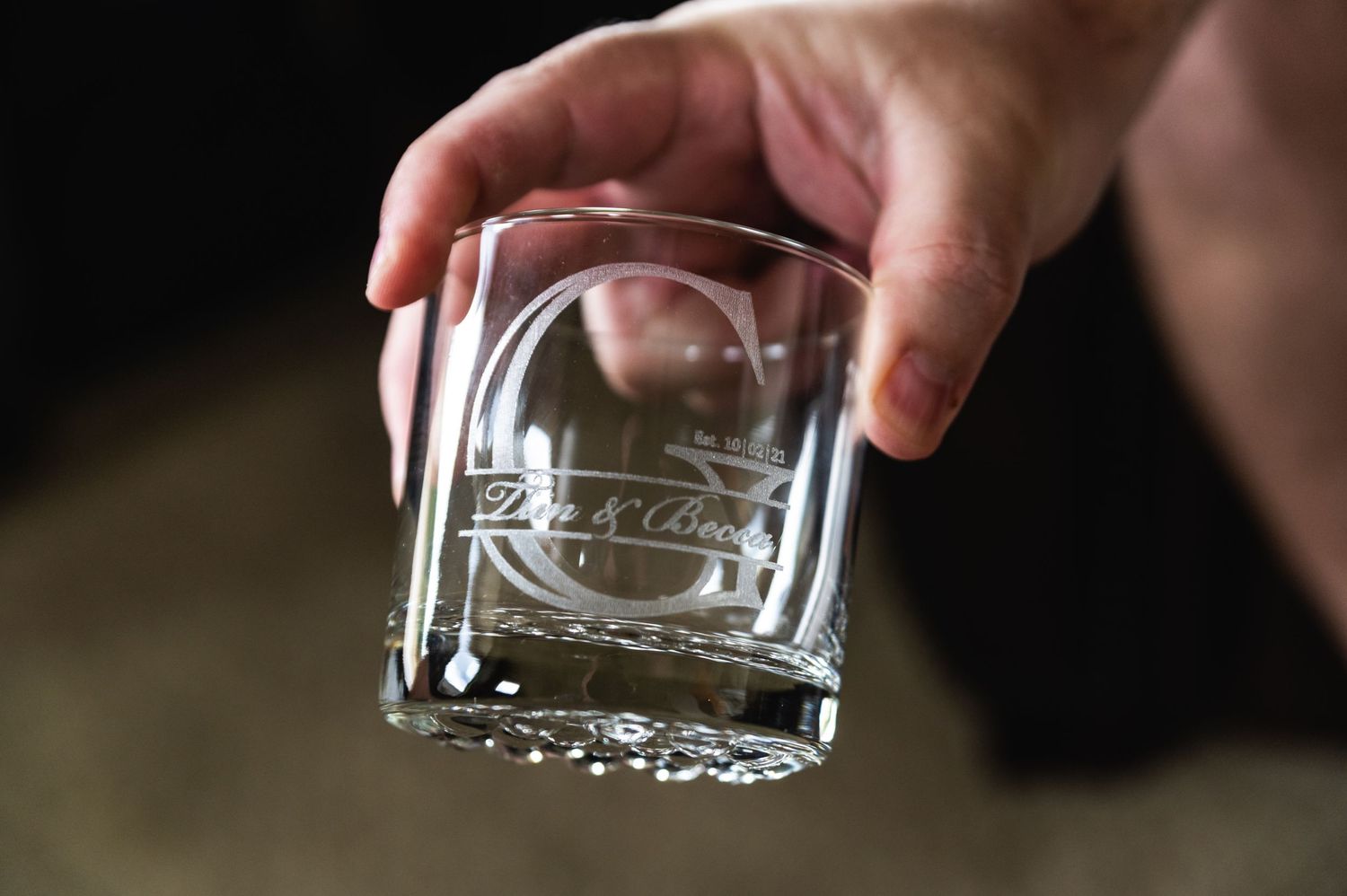 Crystal glass with engraved logo being held up against dark background.