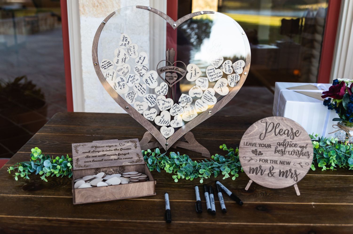 Wedding decor featuring a decorative heart sign and greenery displays on a rustic wooden table.