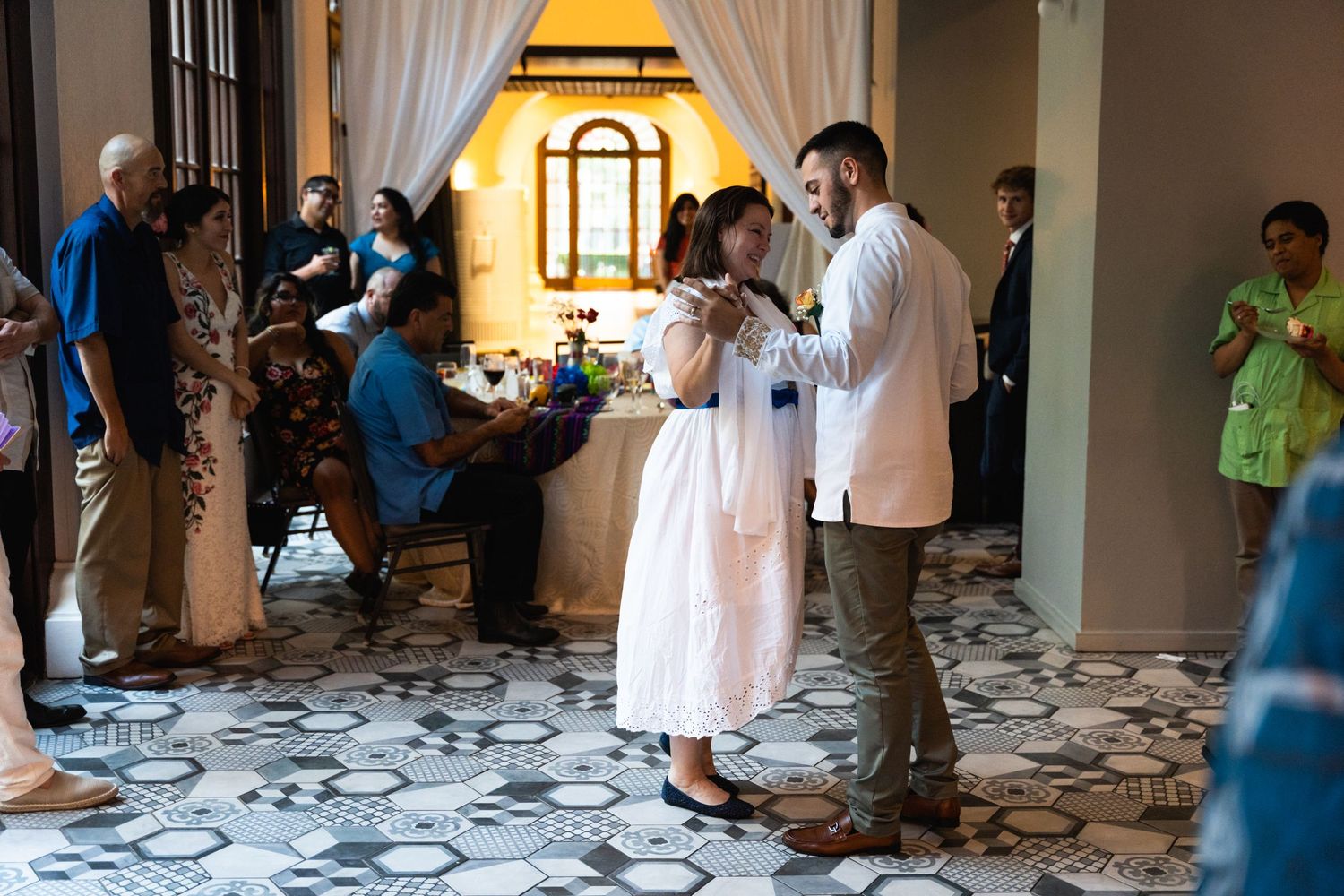 Guests gather and dance in an elegant indoor venue with decorative floor patterns and draped curtains.