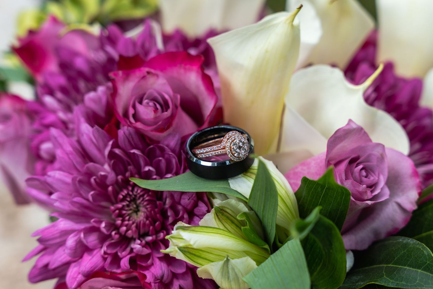 Wedding rings nestled among vibrant pink and white flowers with lush greenery.