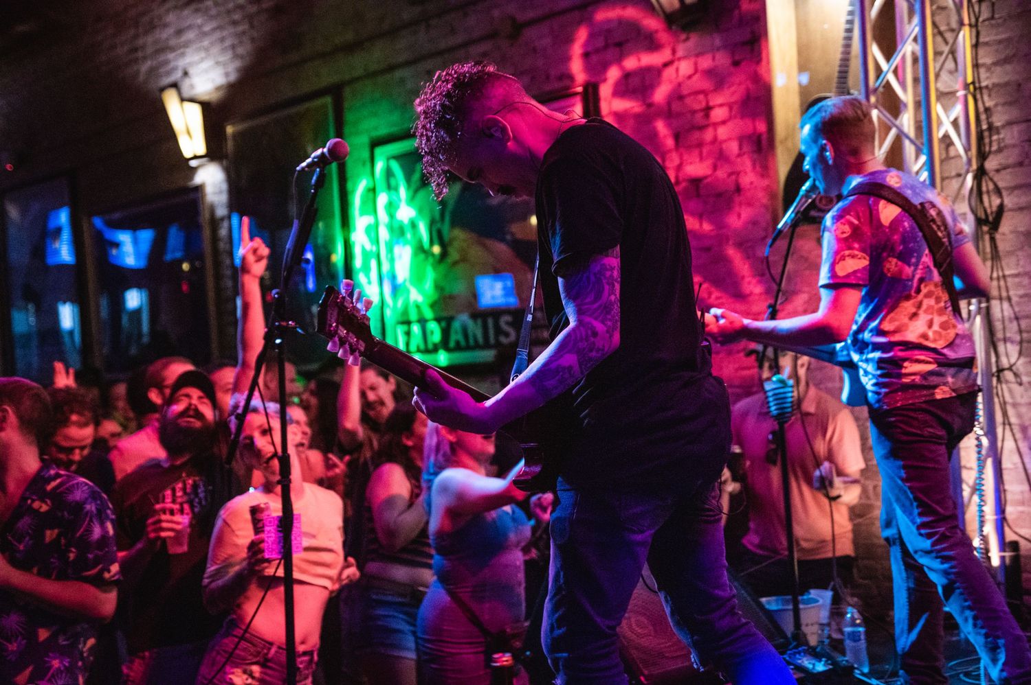 Musicians silhouetted against colorful stage lighting while performing for packed audience.