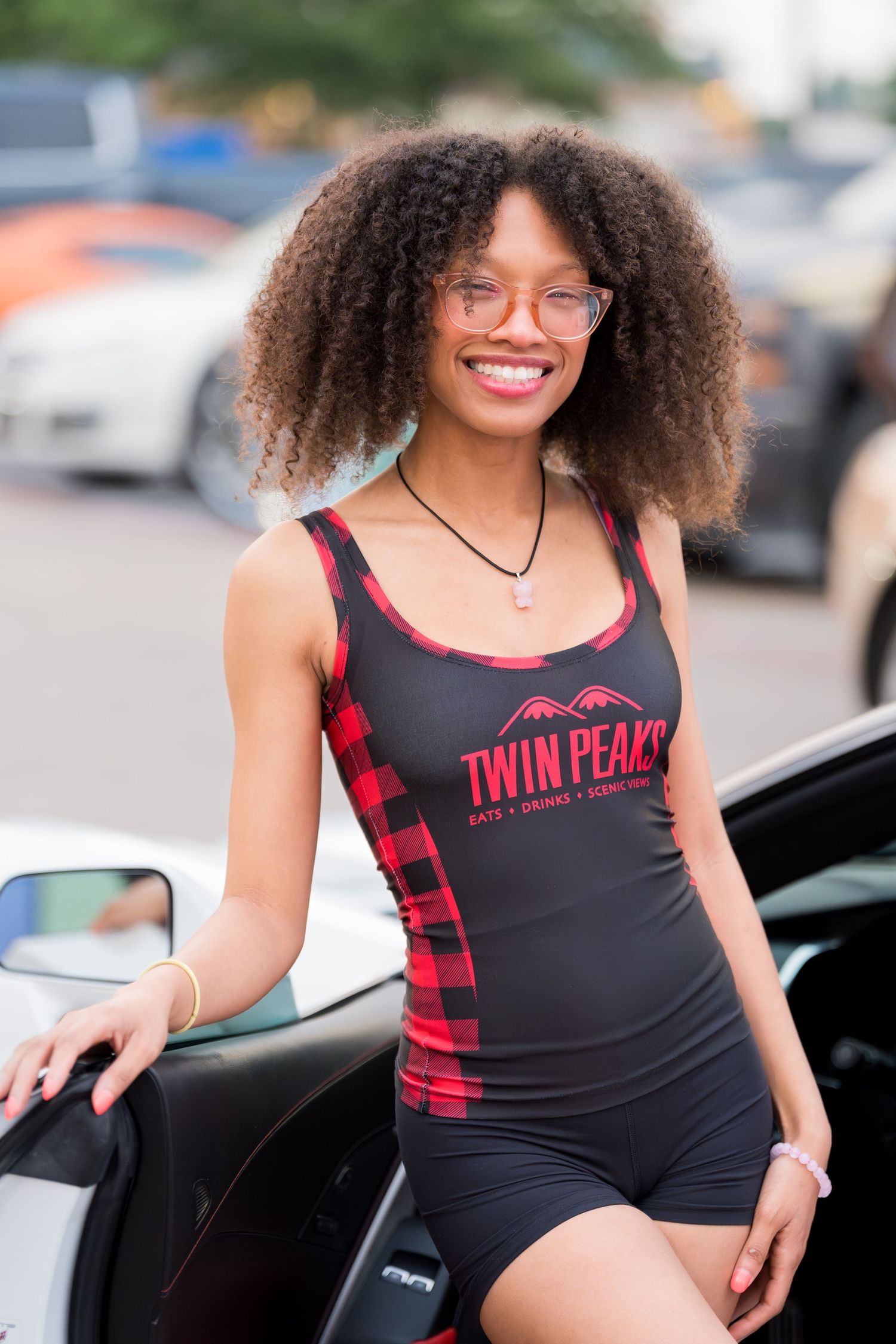 Person wearing glasses and Twin Peaks branded swimsuit poses by car.