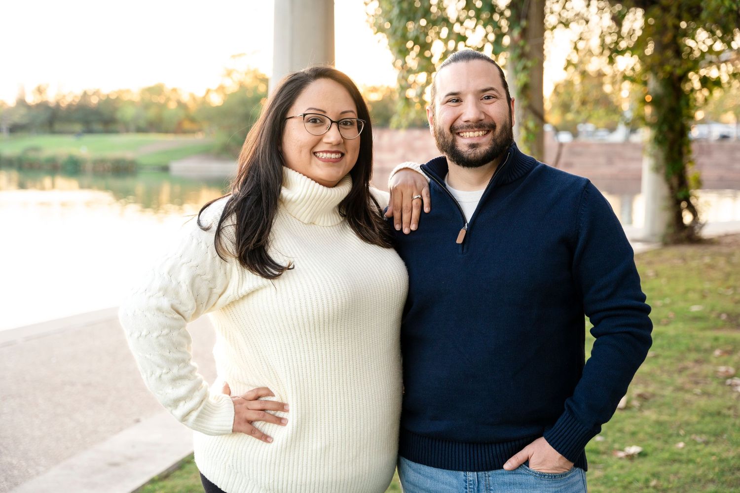 Couple in coordinating sweaters pose together in a park during golden hour.