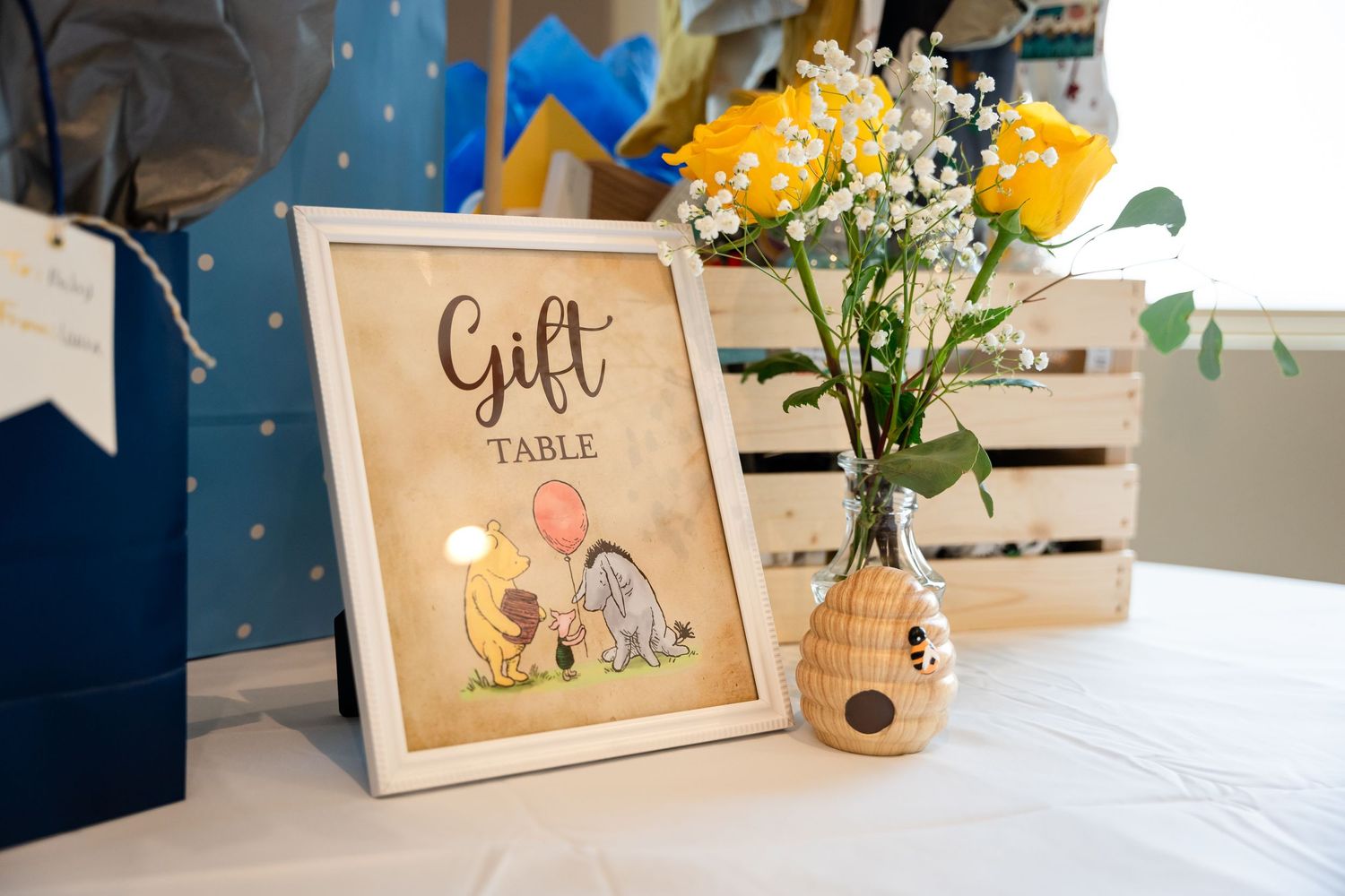 Gift table display with a framed Winnie the Pooh themed sign and yellow flowers in a vase.
