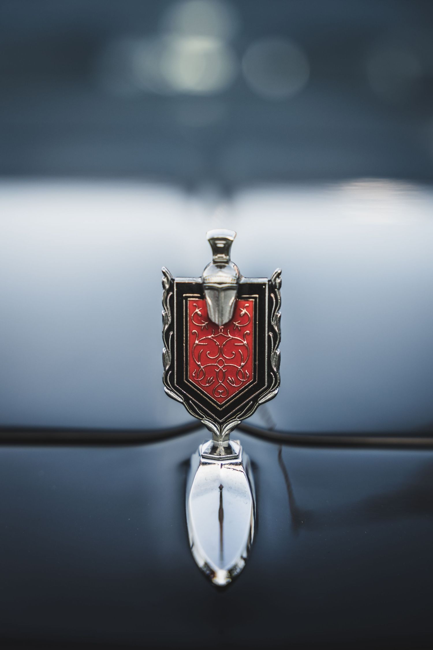 Vintage Pontiac hood ornament featuring red shield emblem against blurred background.