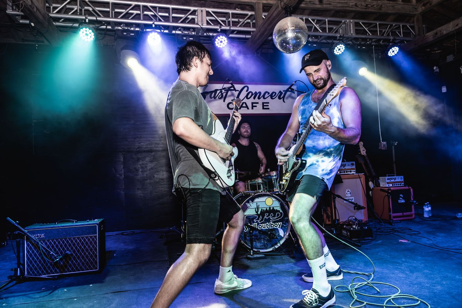 Musicians perform energetically on stage with guitars under blue lighting.