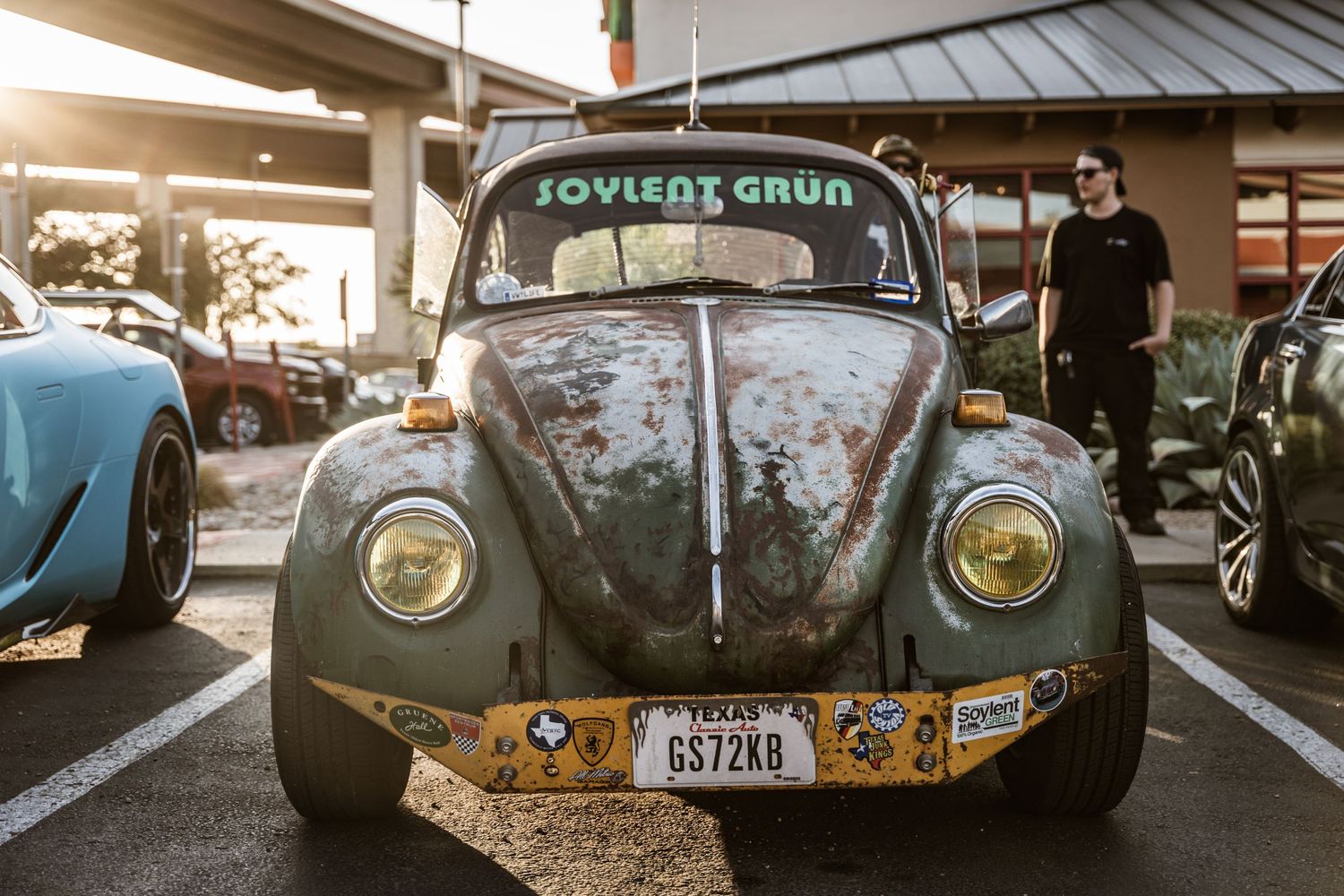 Weathered Volkswagen Beetle with stickers and patina finish at a car meet.