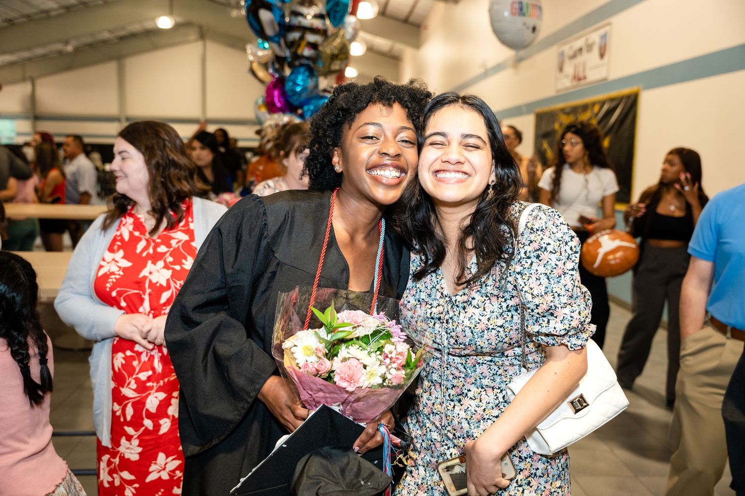 Two people embrace while holding flowers and celebrating at graduation.