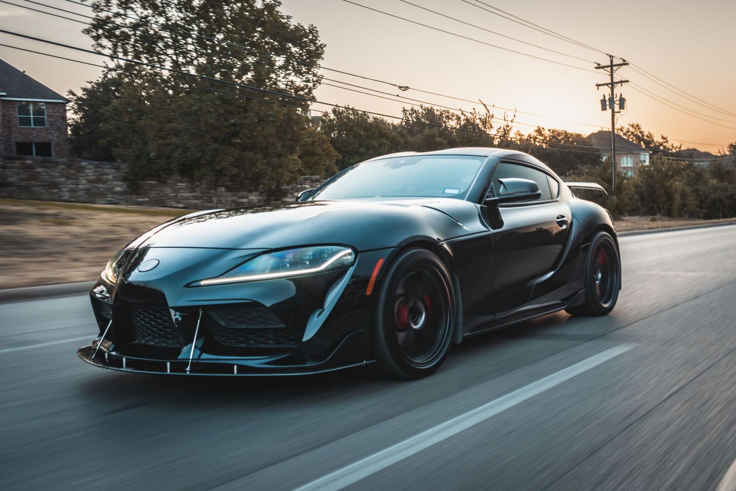 Black widebody Toyota Supra with custom aero kit driving at dusk.