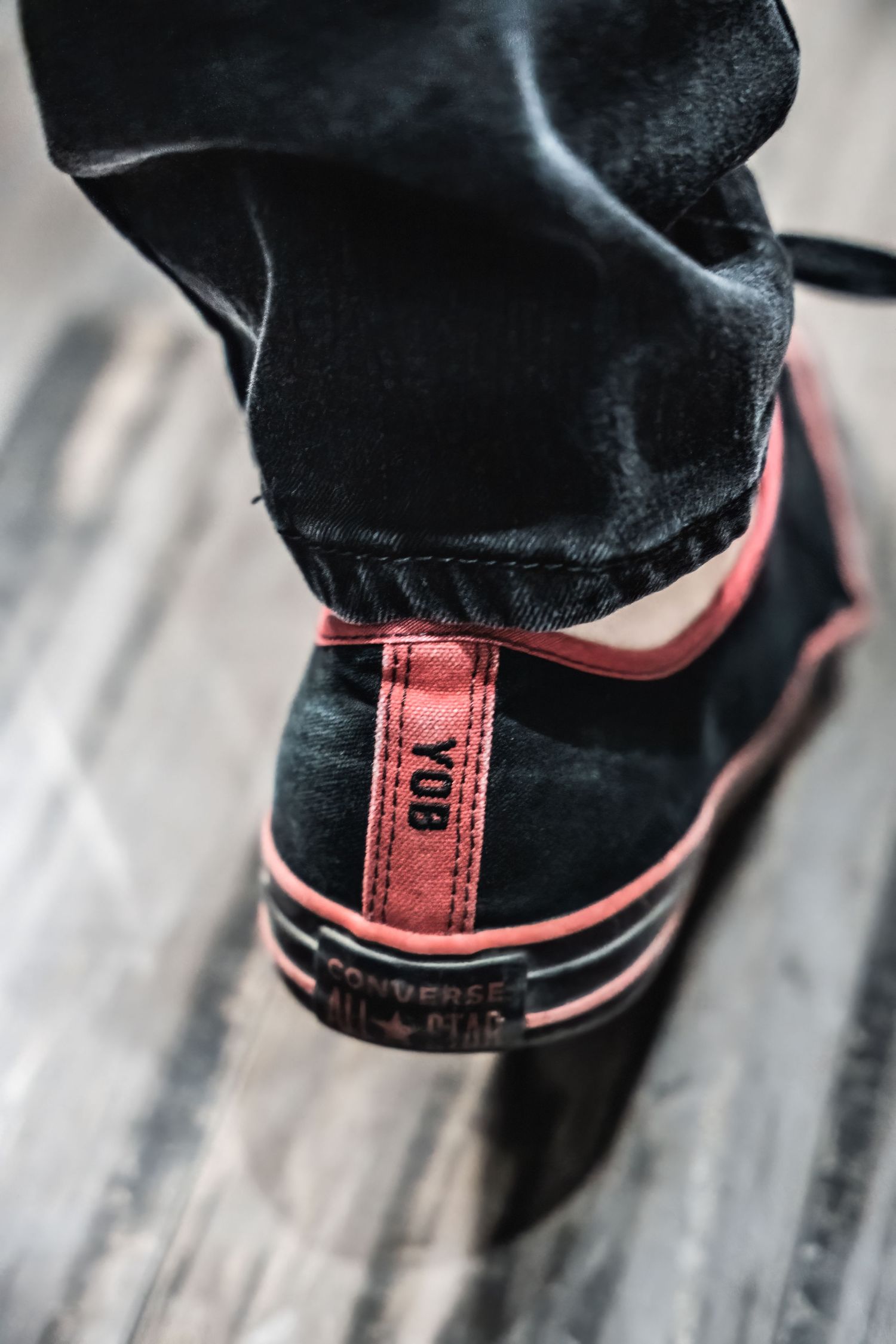 Close-up detail shot of black and red sneaker on wooden flooring.