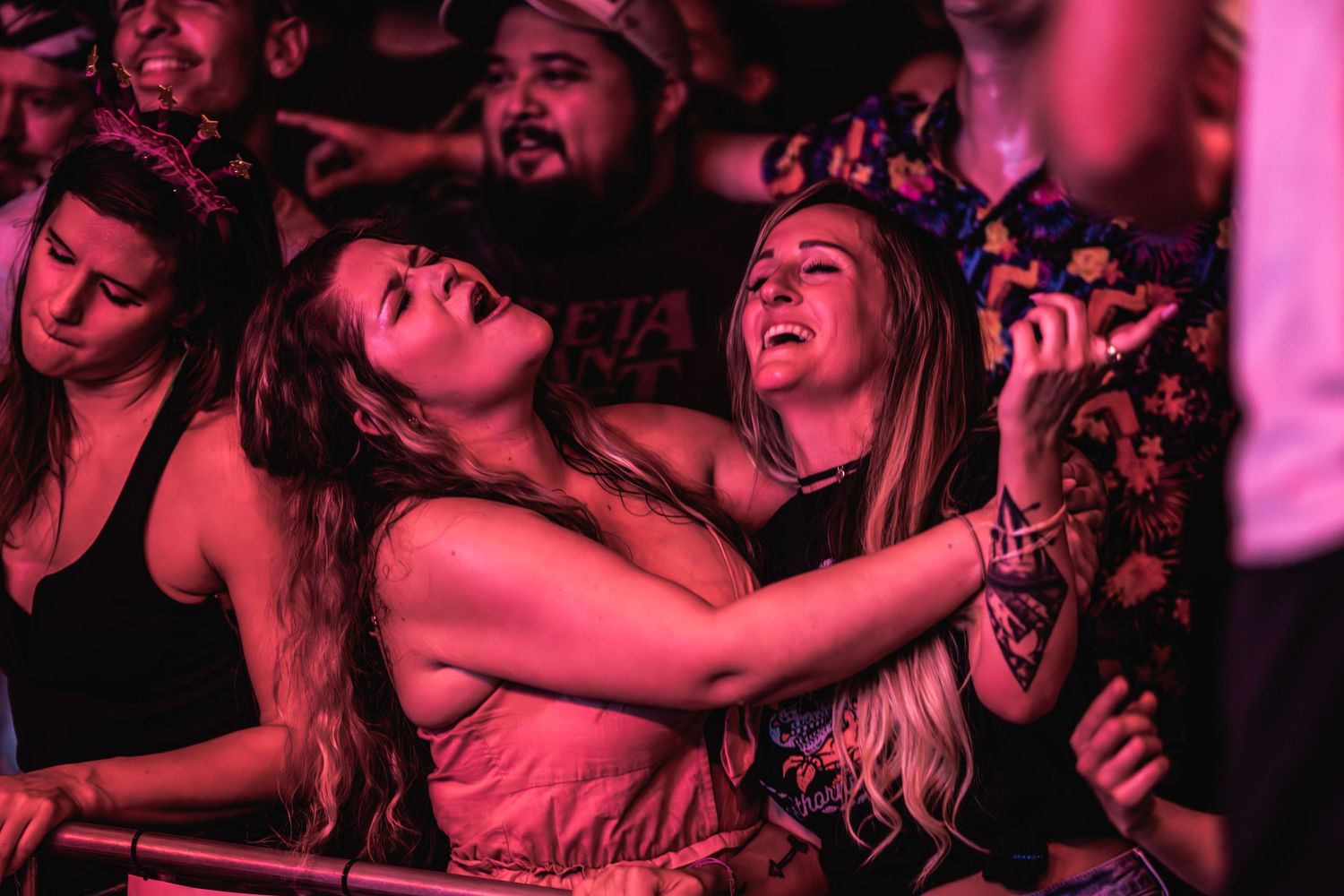 Concert attendees dancing and celebrating under pink mood lighting at music event.
