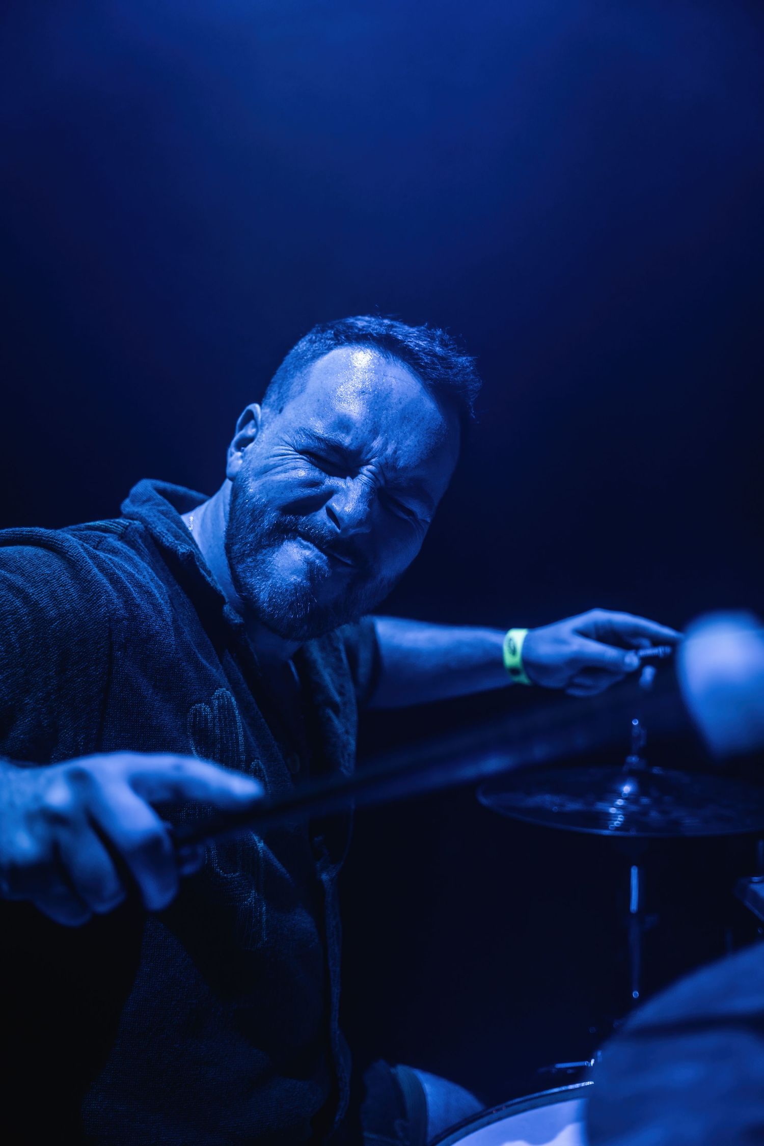 Dramatic blue-lit shot of drummer mid-performance on stage.
