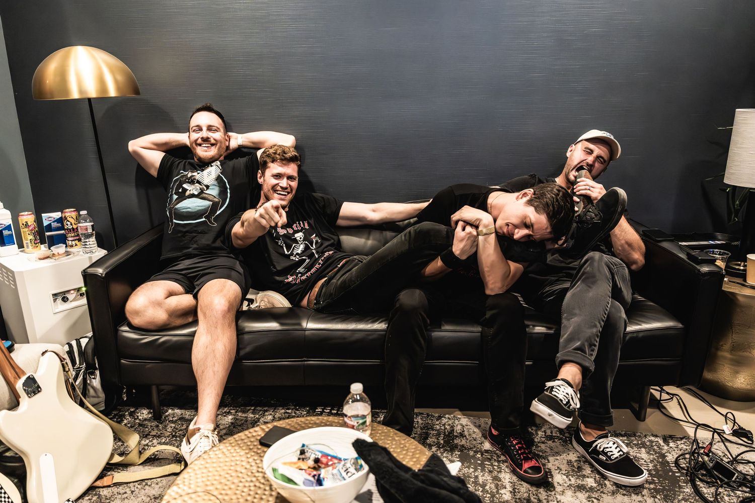 Band members relax together on a black leather couch backstage making silly faces for the camera.