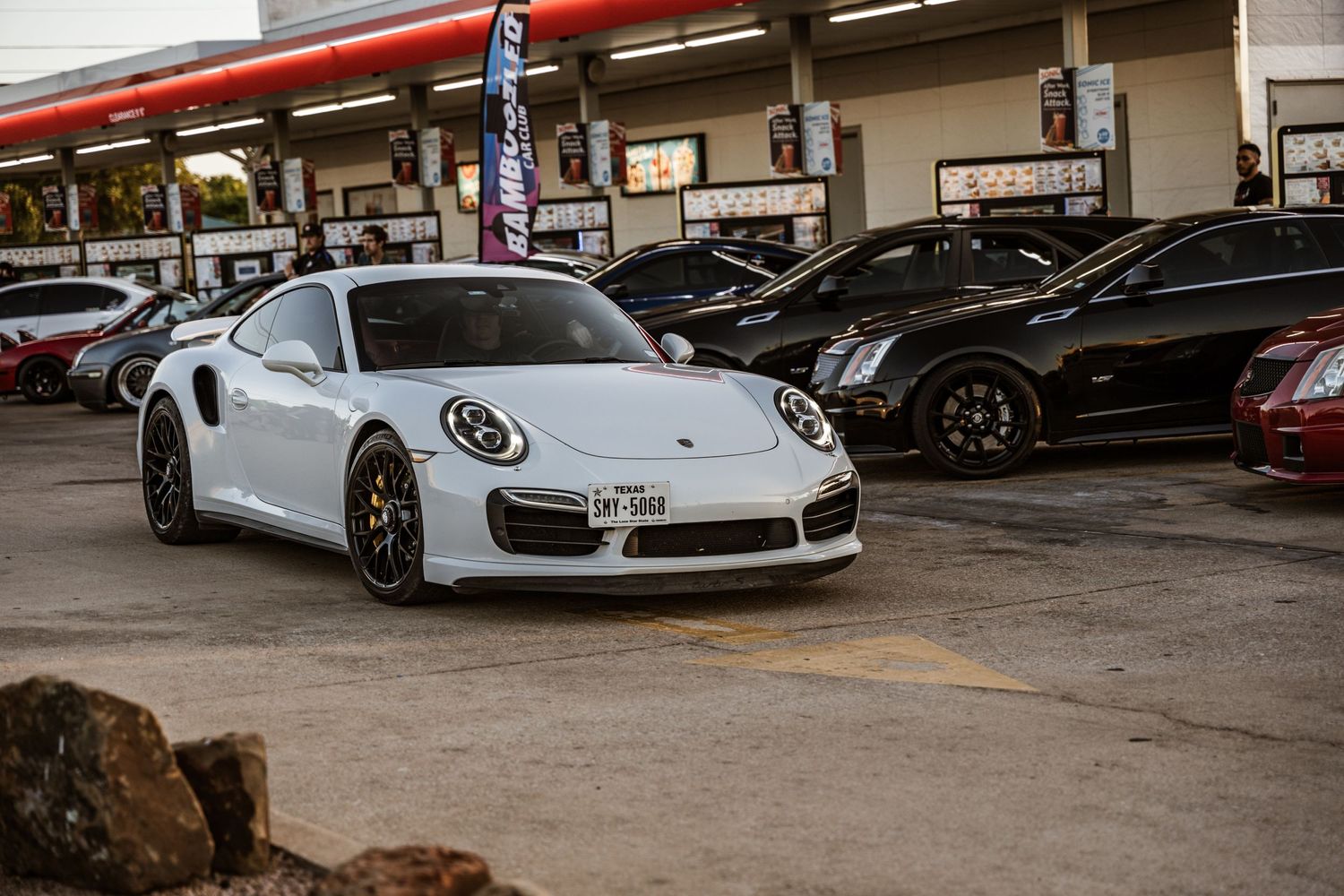 White Porsche 911 Turbo parked in a gas station lot with aftermarket wheels.