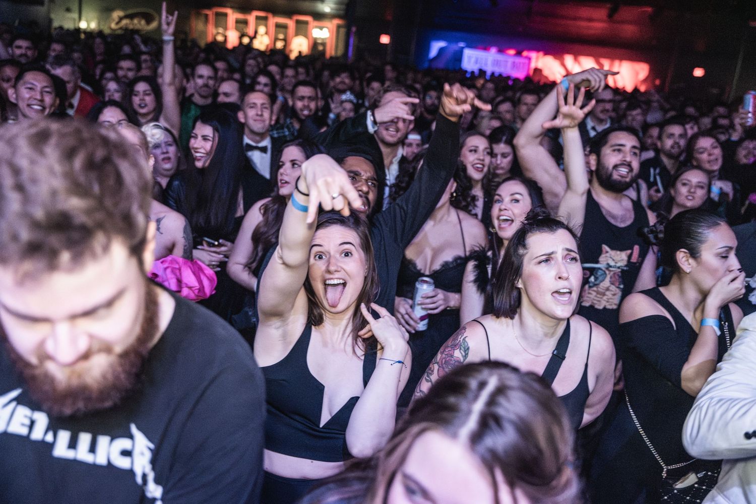 Enthusiastic concert crowd cheering with raised hands at music venue.