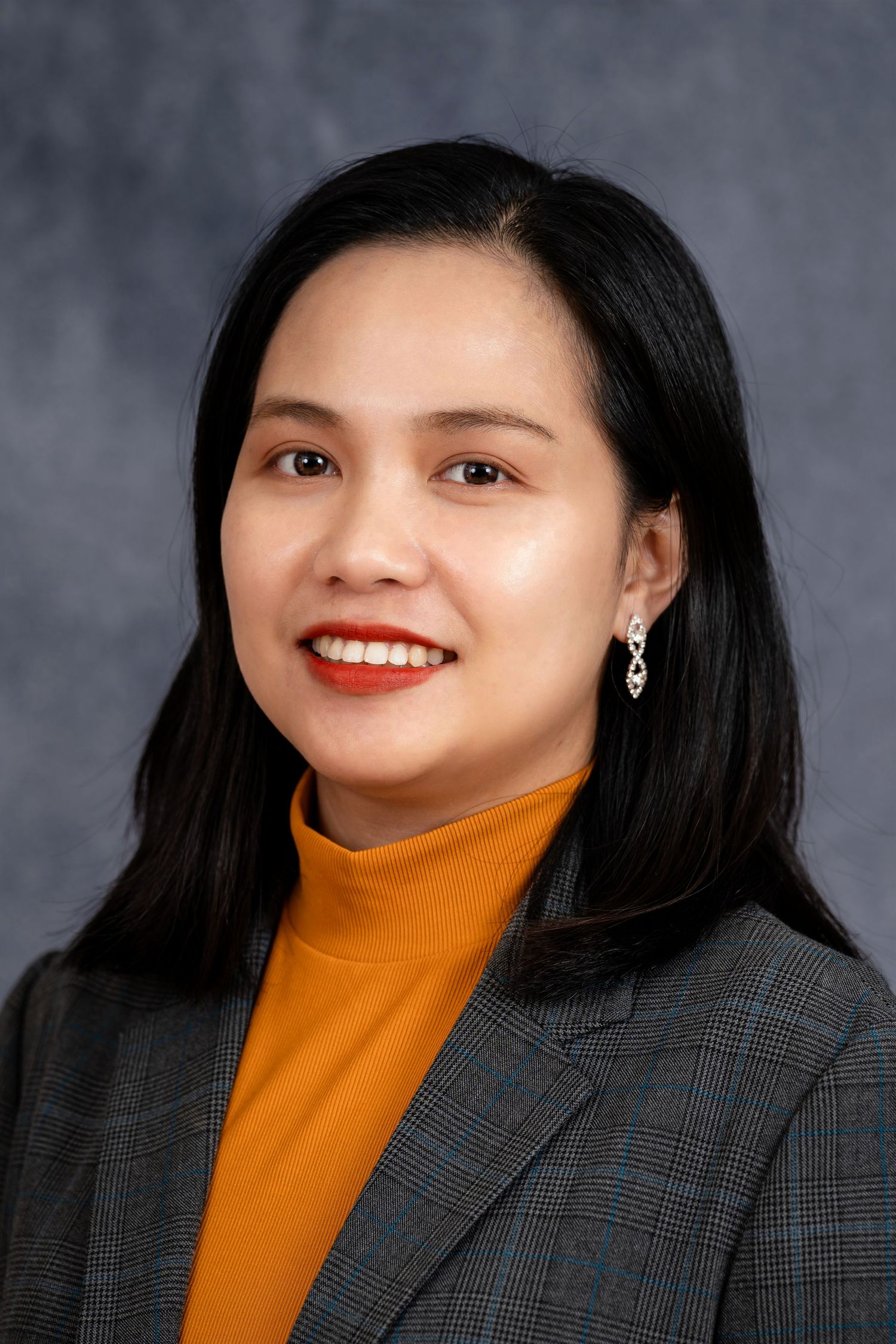 Professional portrait of a person wearing an orange turtleneck and plaid blazer.