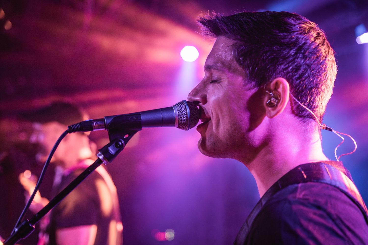 Singer passionately performs at a concert with dramatic purple and pink stage lighting.