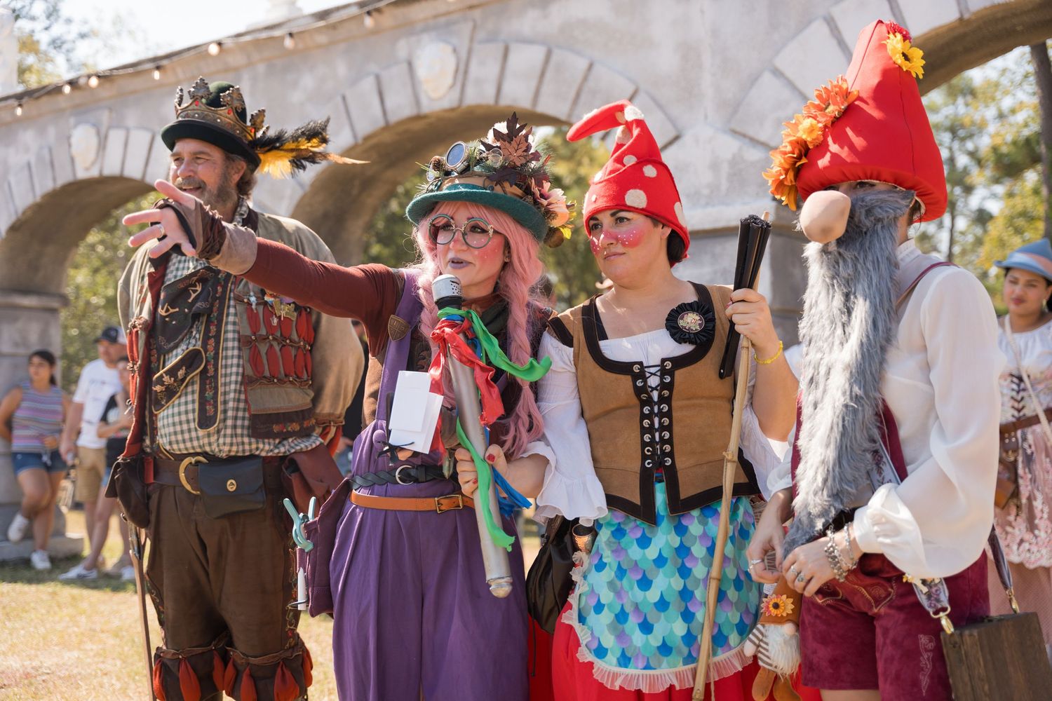 Festival entertainers in period dress perform together under stone arches outdoors.