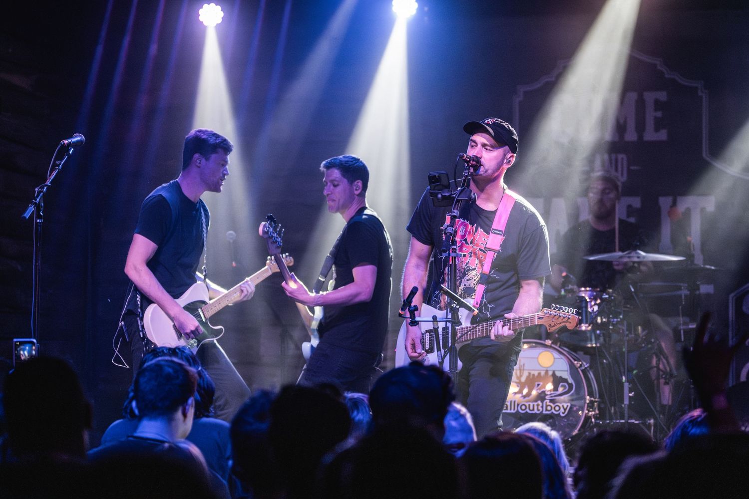 Three musicians perform together on stage under bright white spotlights.