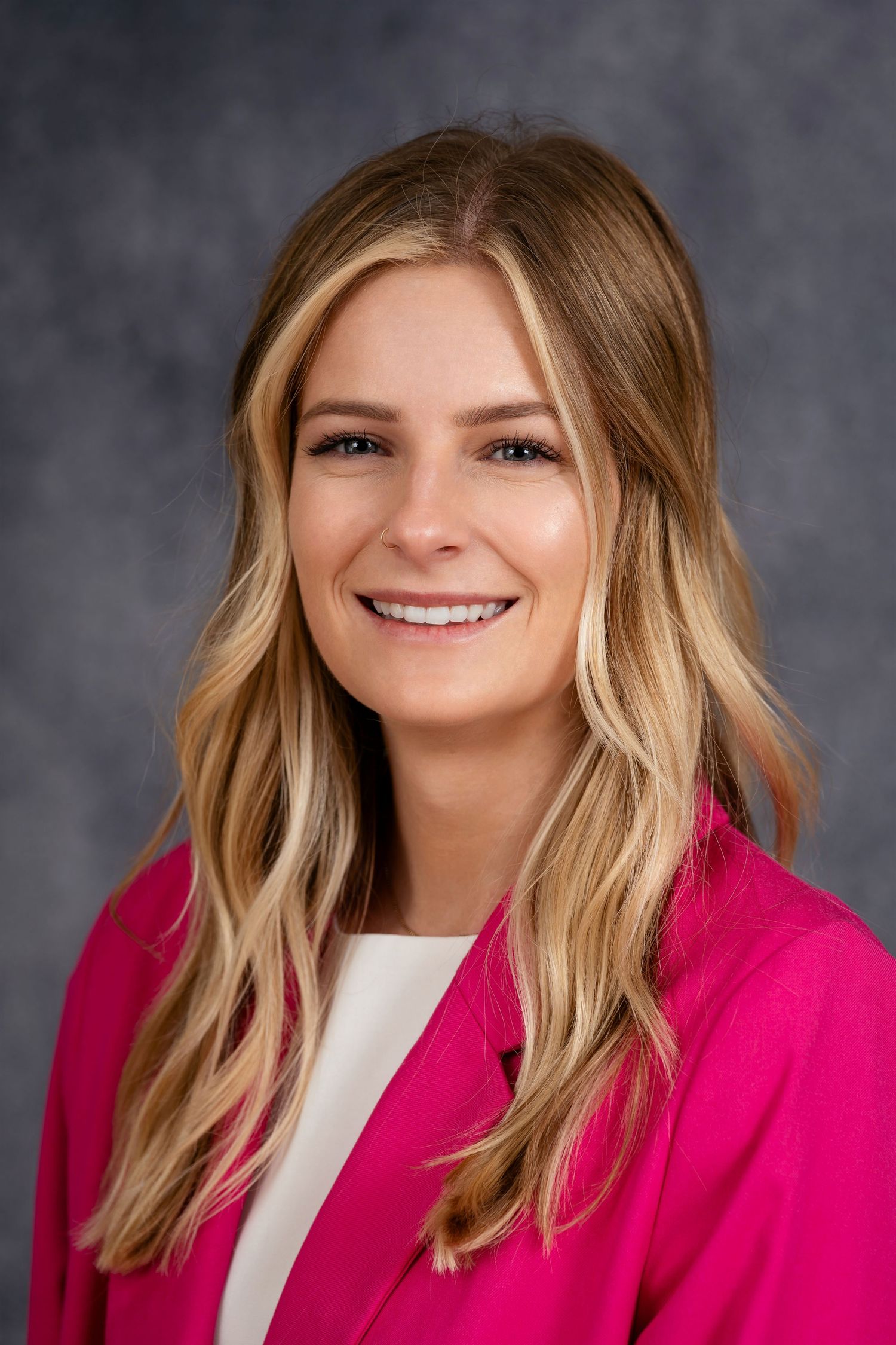 Professional headshot featuring bright pink blazer and wavy blonde hair.