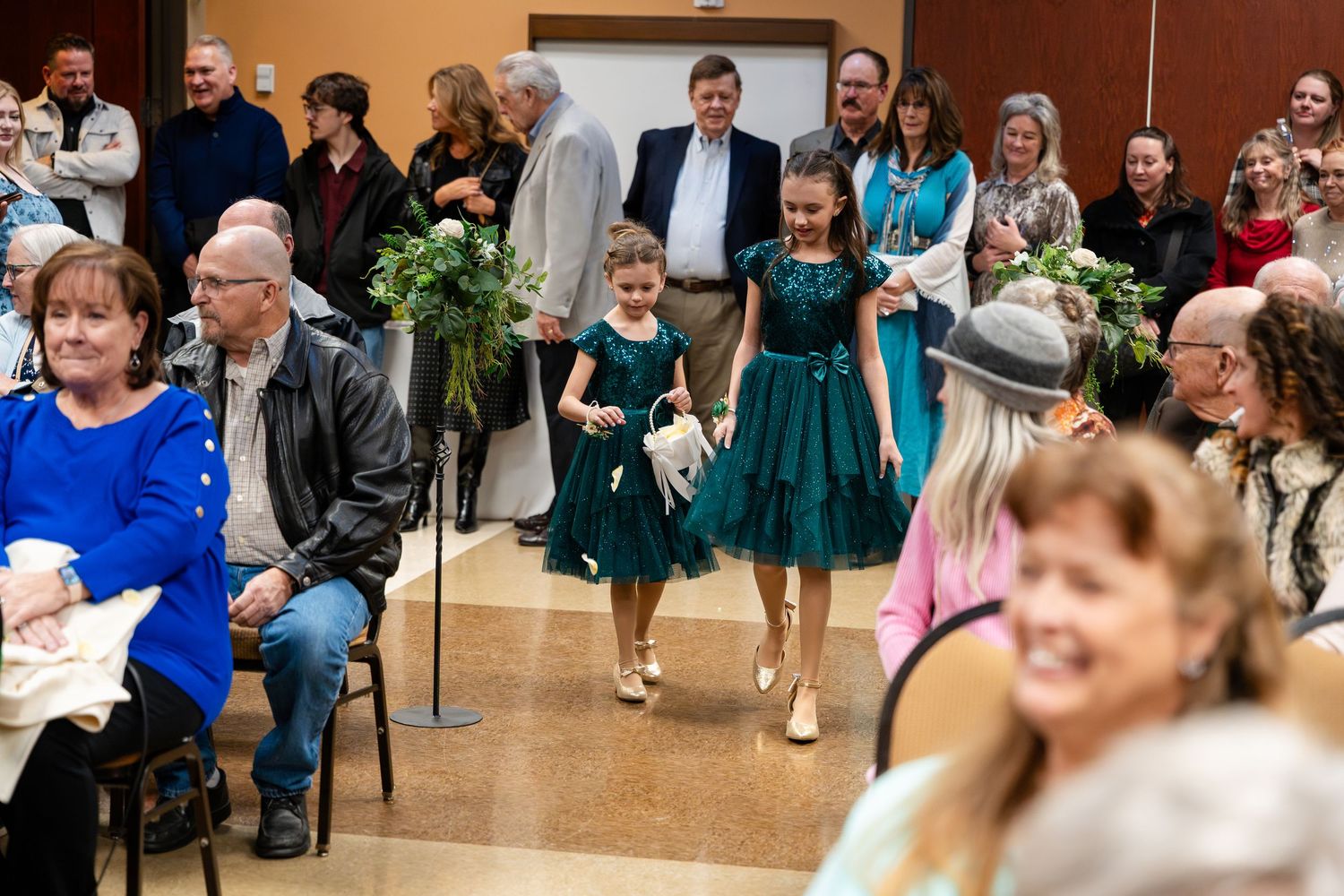 People at a formal event wearing blue and turquoise dresses gather in a reception hall.