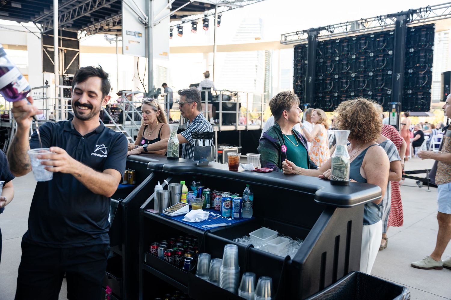 Bartender serving drinks at outdoor bar setup with blue glassware.