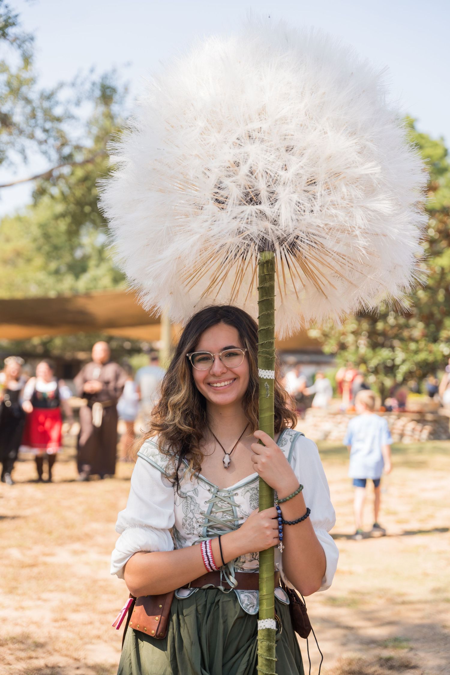 A festival attendee holding a giant dandelion prop at a renaissance fair.