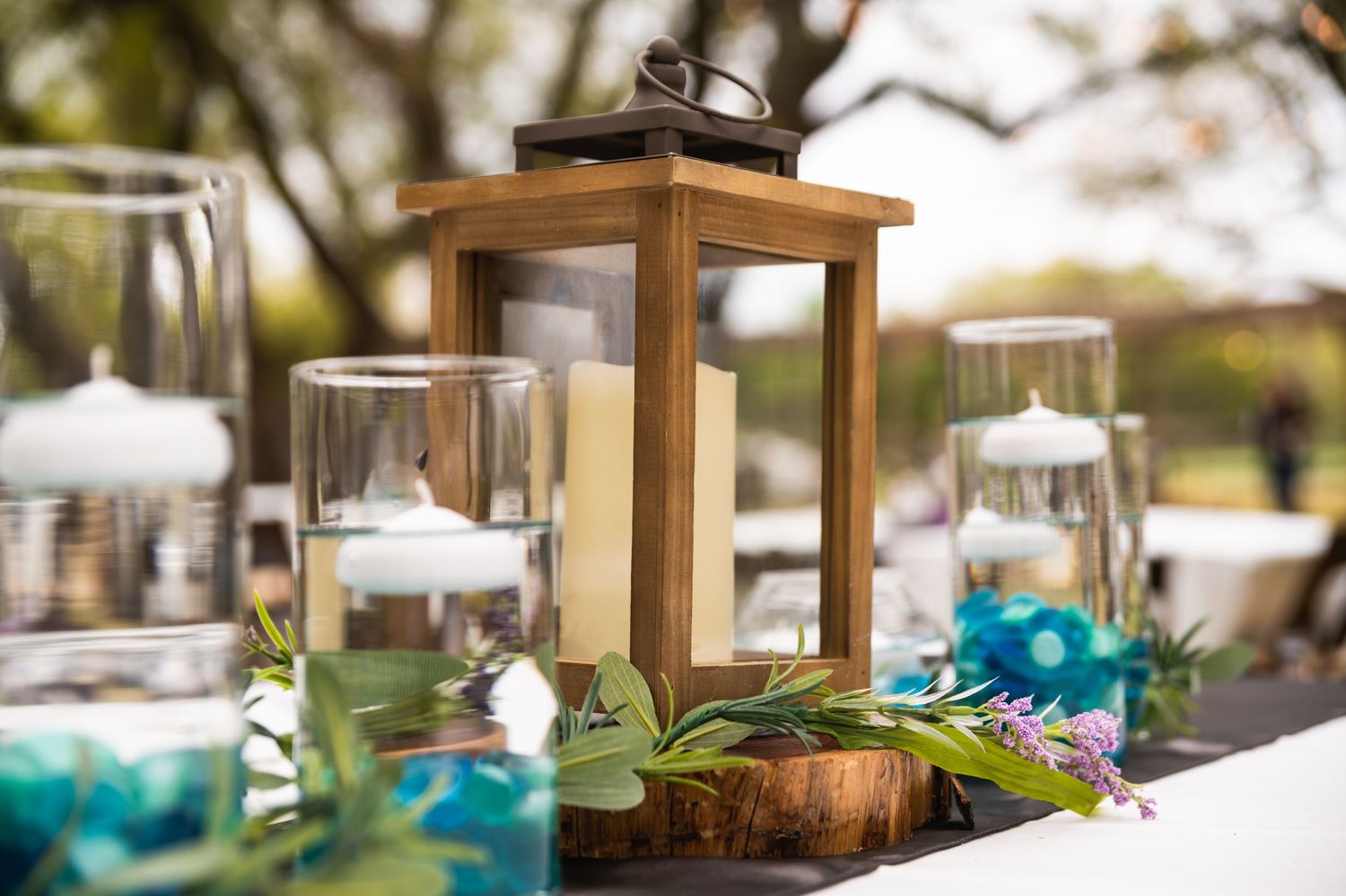 Rustic wooden lantern centerpiece with teal glassware on decorated table.