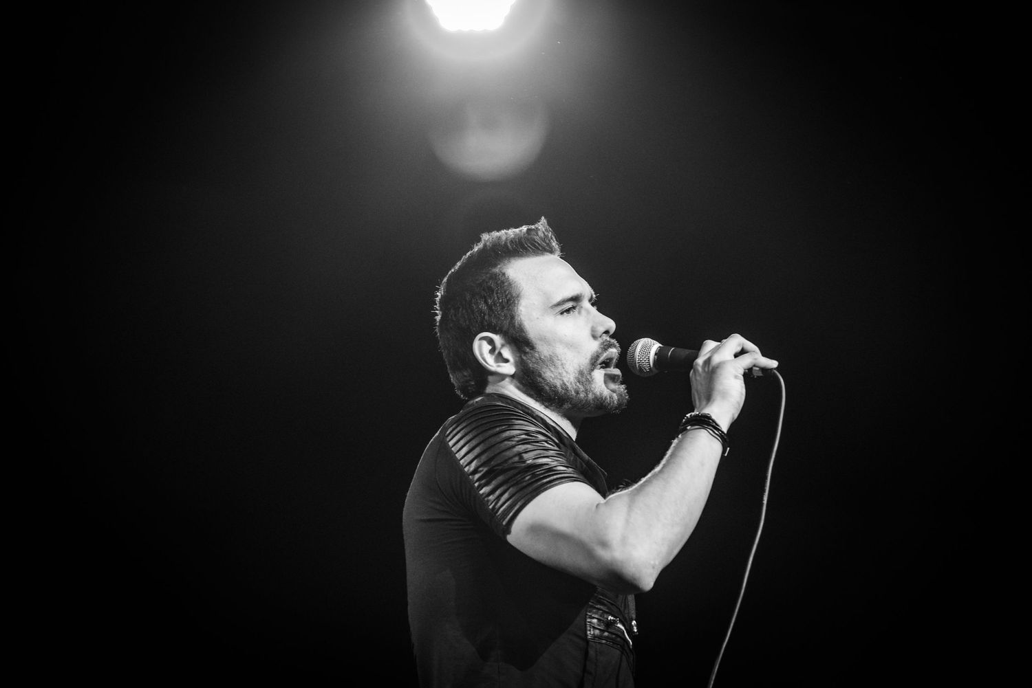 Concert performer sings passionately into microphone during dramatic black and white stage performance.