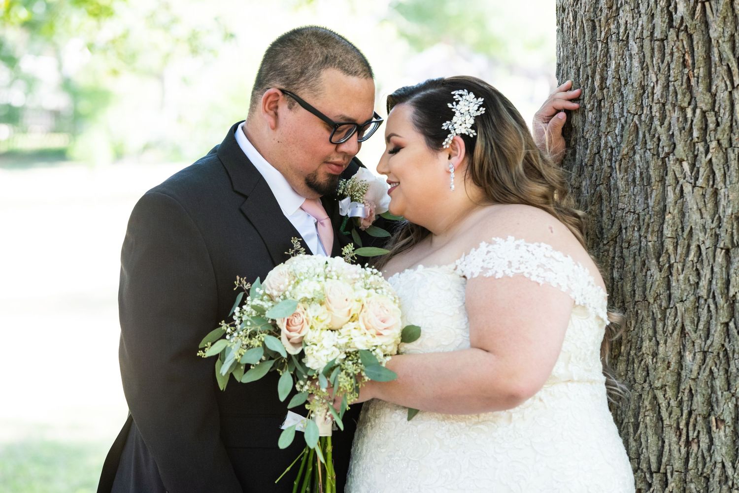 Romantic wedding portrait of couple by tree with cream and green floral bouquet.