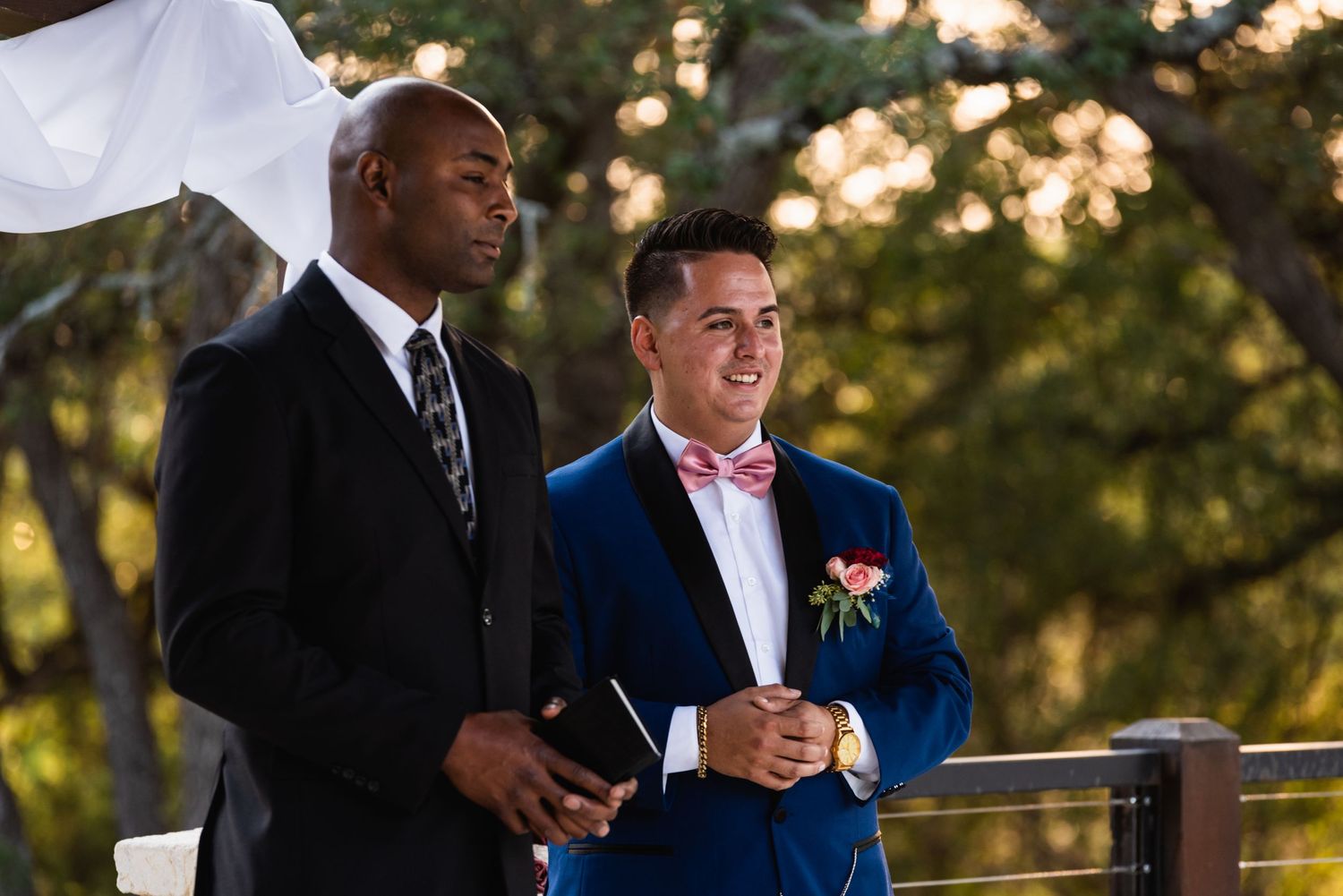 Two people watch intently during an outdoor ceremony in formal attire.