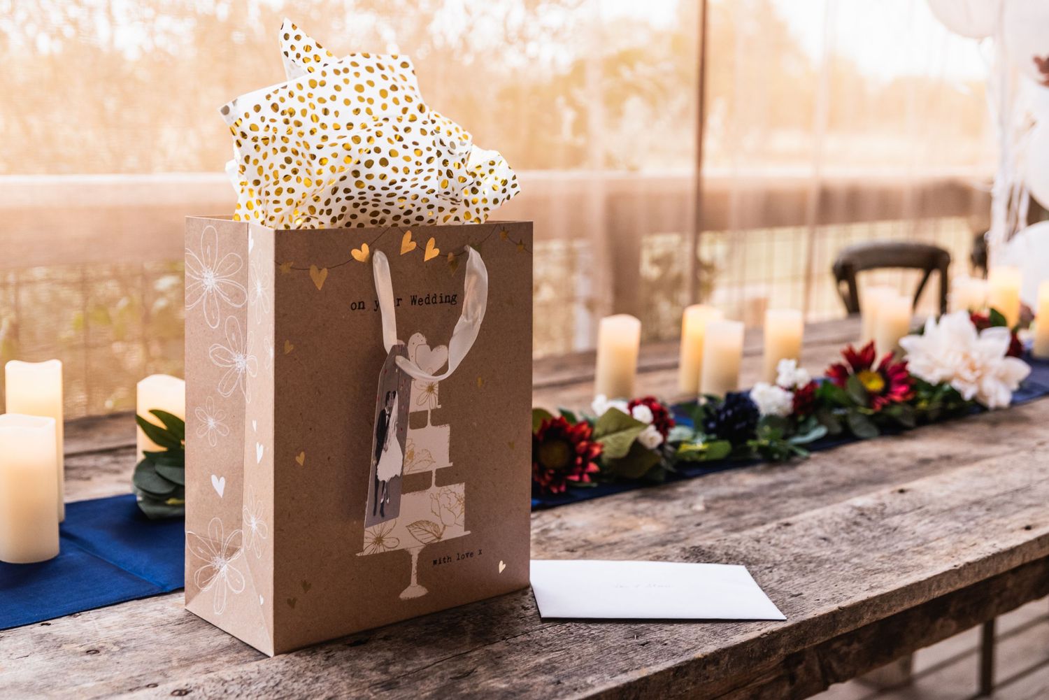 A decorative gift bag with star pattern sits on a rustic table with candles and floral arrangements.