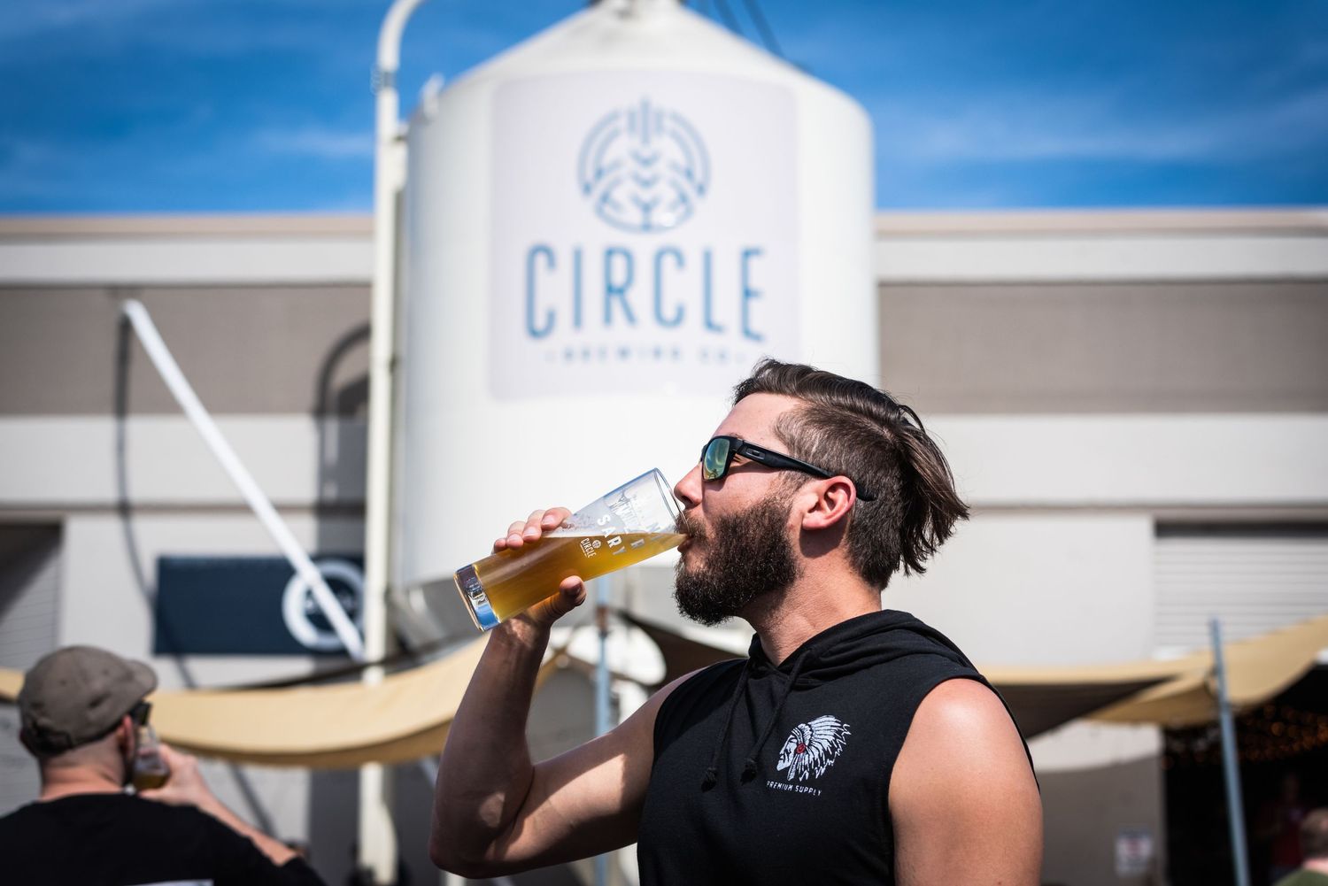 Person drinking a beer in front of Circle Brewing Company's storage tank.